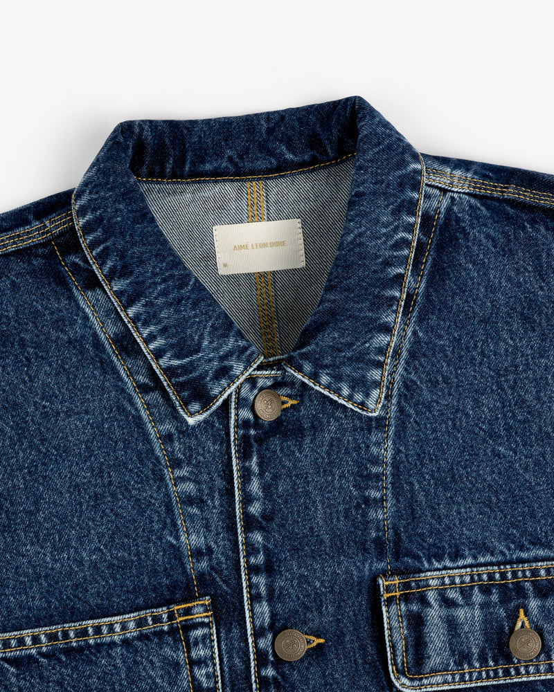 Close-up of the Denim Trucker Jacket in blue with two chest pockets and visible stitching.