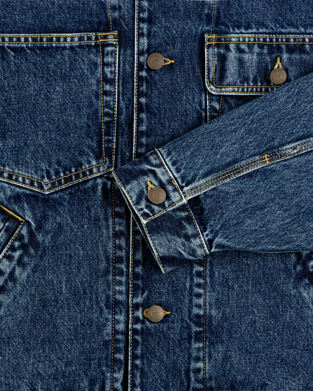Close-up of the Denim Trucker Jacket featuring buttons, stitching, pockets, and a sleeve draped across the front.
