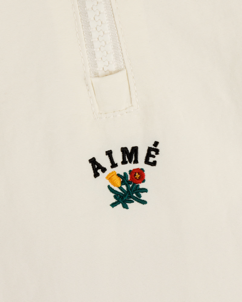 Close-up of the Crest Nylon Half-Zip Pullover with AIMÉ embroidered above two small yellow and red flowers.
