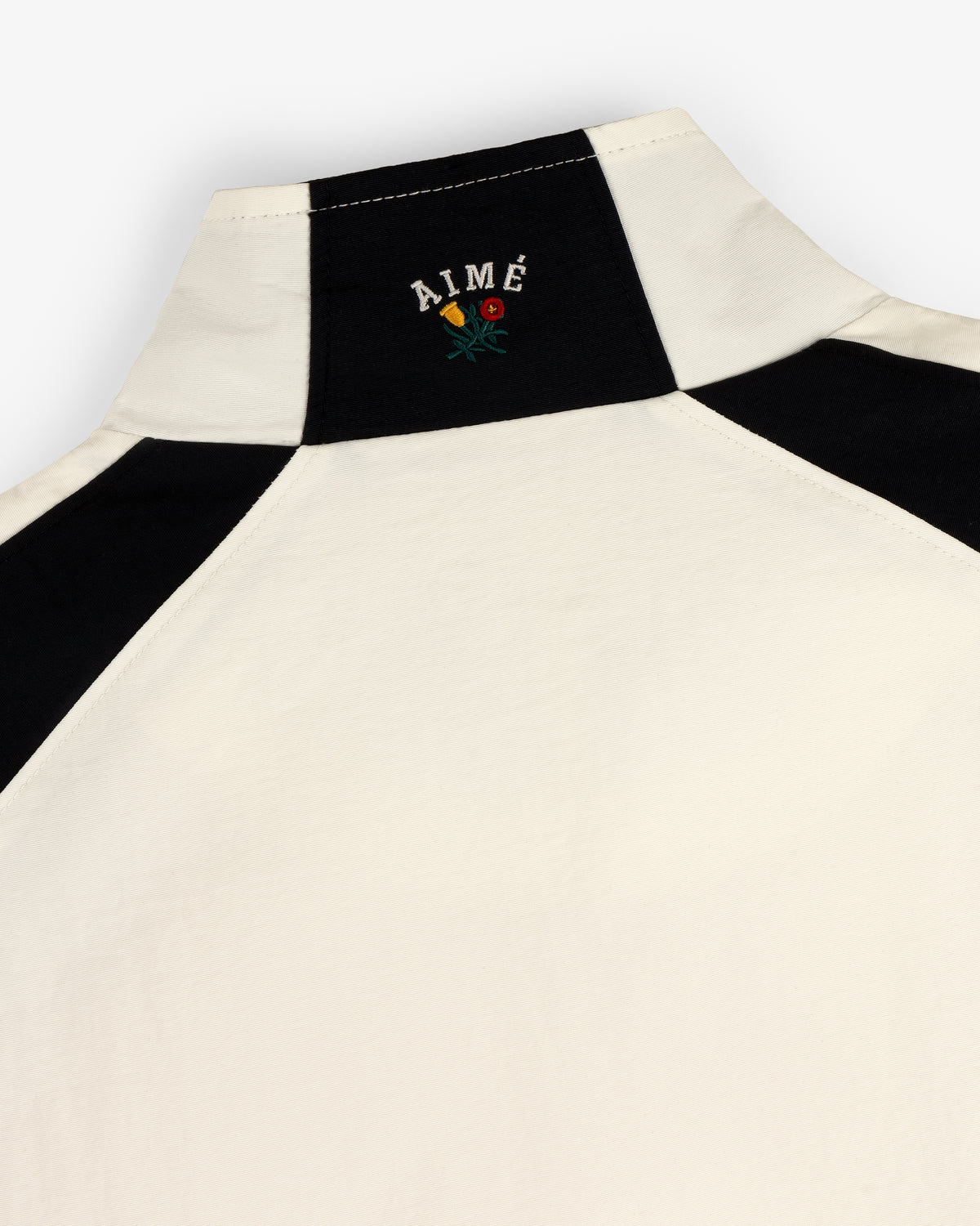 Crest Nylon Half-Zip Pullover in white and black with 'AIMÉ' and a small embroidered flower on the back collar.