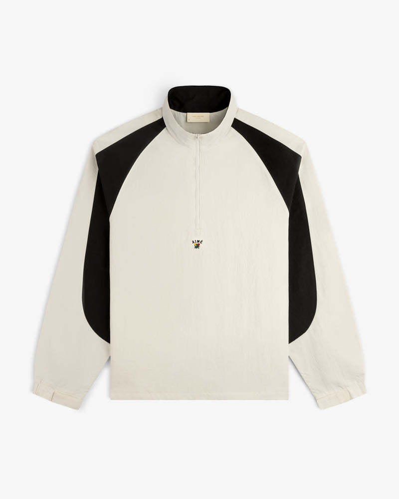 Crest Nylon Half-Zip Pullover: cream long-sleeve with black shoulders, quarter zip, and small embroidered bee on chest.
