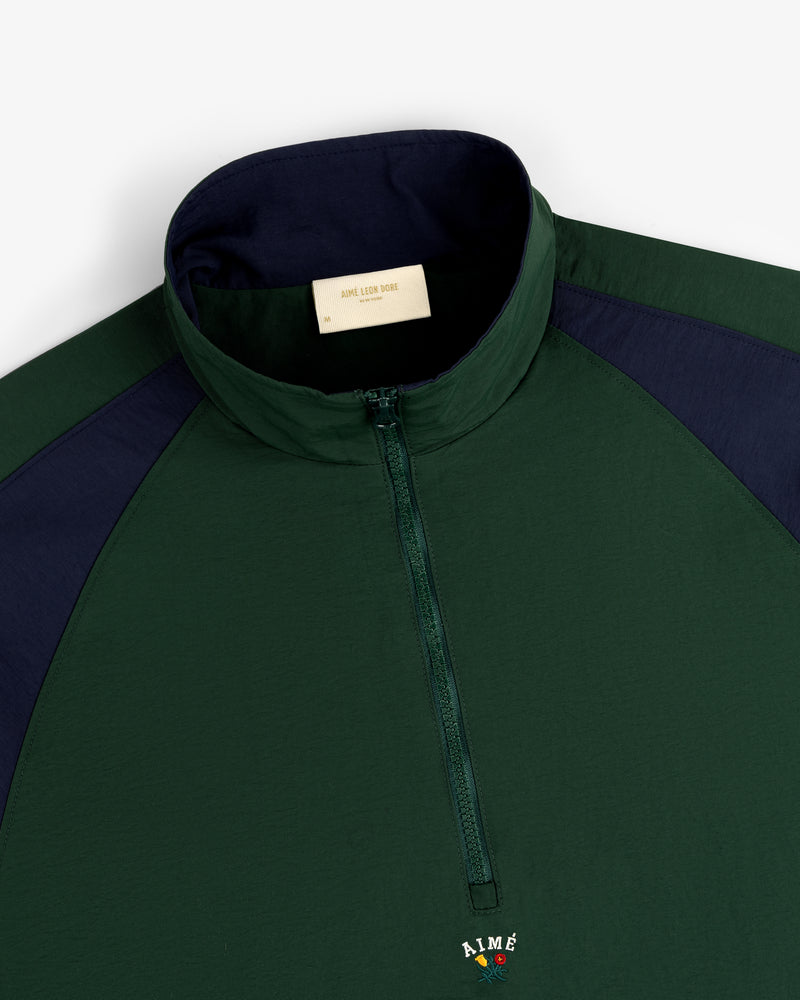 The Crest Nylon Half-Zip Pullover in dark green and navy features a stand collar and AIME logo below the zipper.
