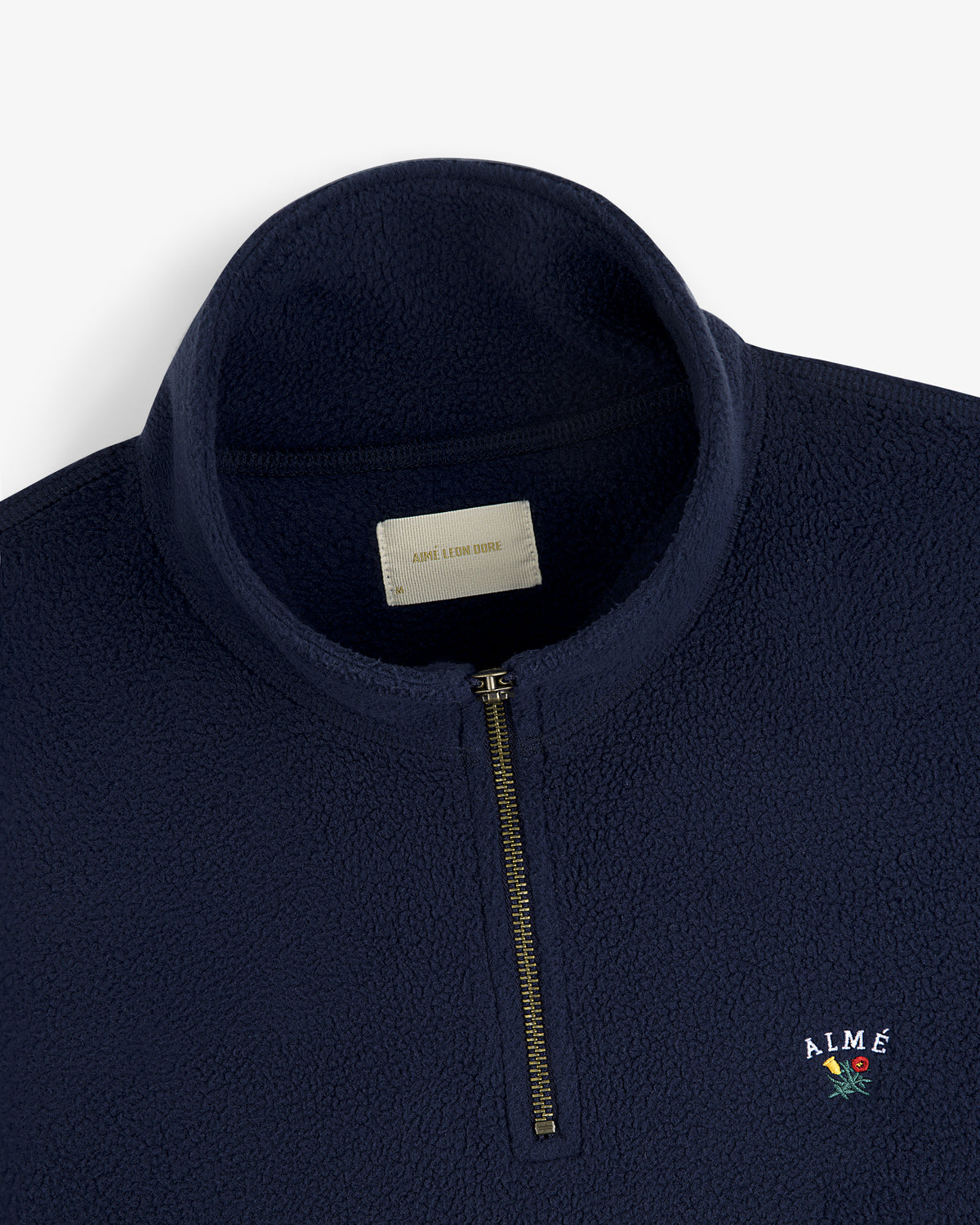 Crest Quarter-Zip Fleece Pullover in navy with ALMÉ logo and a small embroidered flower near the chest.