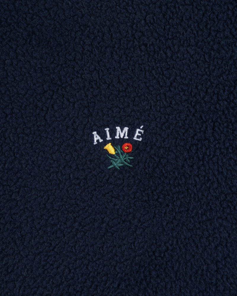 Navy Crest Quarter-Zip Fleece Pullover with AIMÉ embroidered above a yellow and red flower.