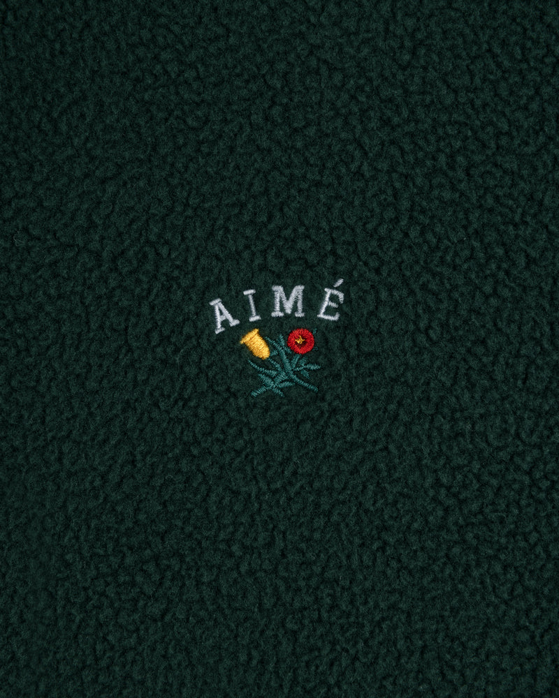 Dark green Crest Quarter-Zip Fleece Pullover with AIMÉ embroidered above yellow and red flowers with green stems.