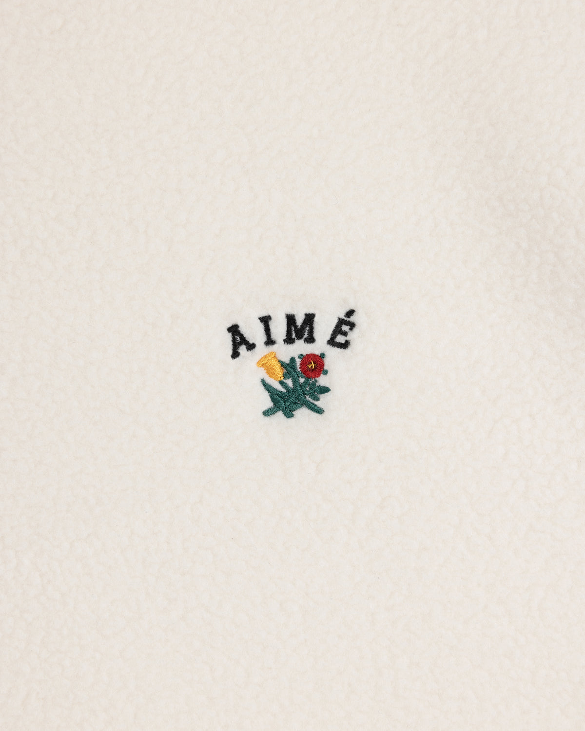 White Crest Quarter-Zip Fleece Pullover with AIMÉ embroidered above a small yellow and red flower with green leaves.