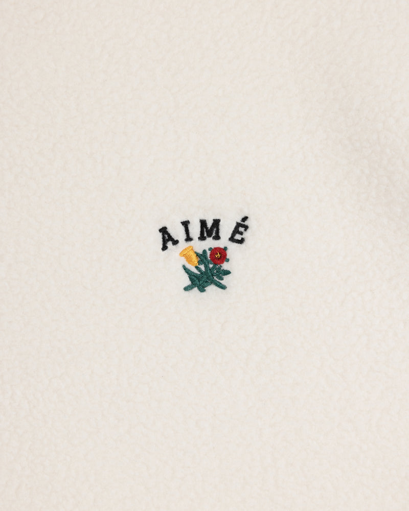 White Crest Quarter-Zip Fleece Pullover with AIMÉ embroidered above a small yellow and red flower with green leaves.