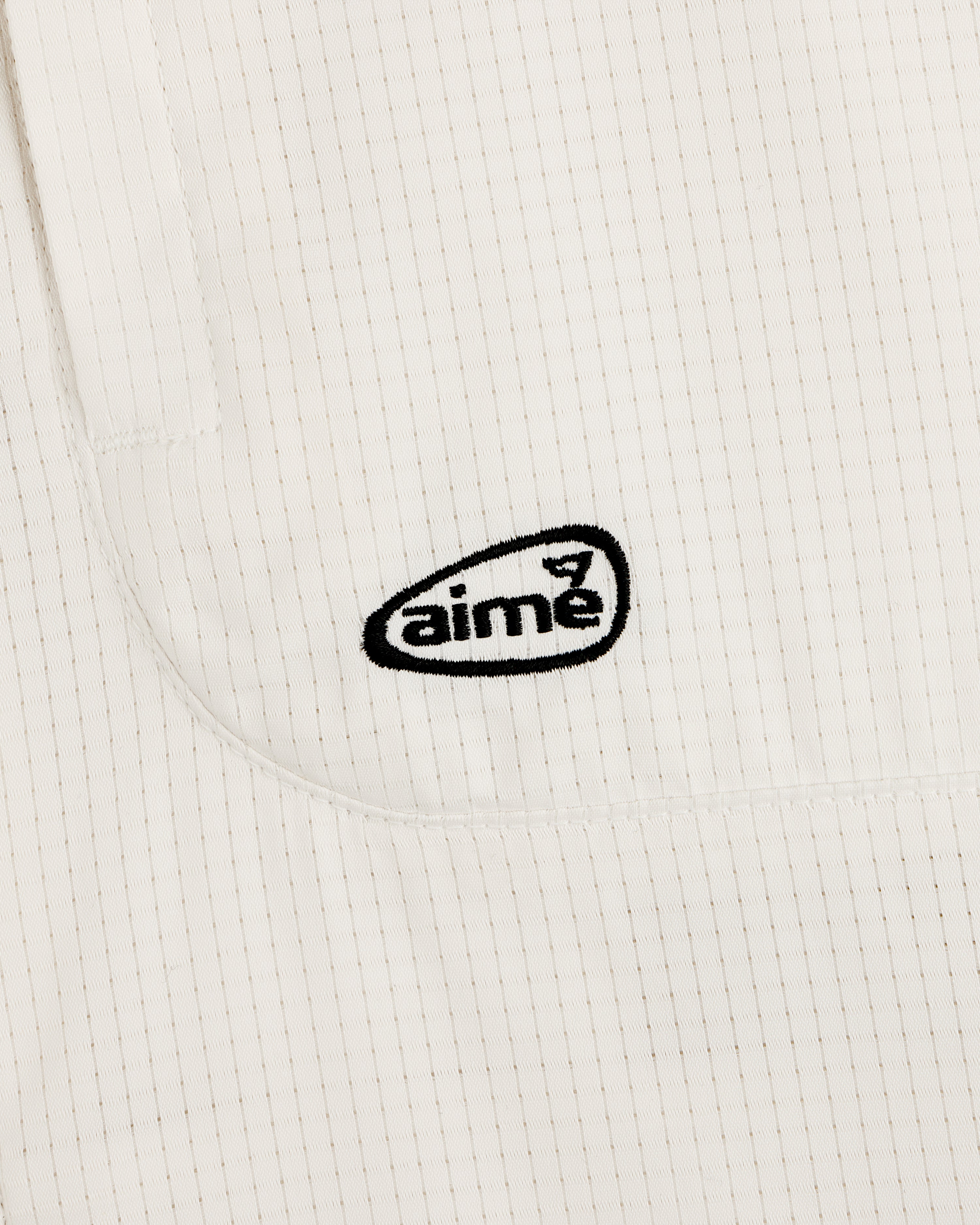 Close-up of the ALD Golf Lightweight Tips Windbreaker: white fabric with thin vertical stripes and black aimé logo embroidery.