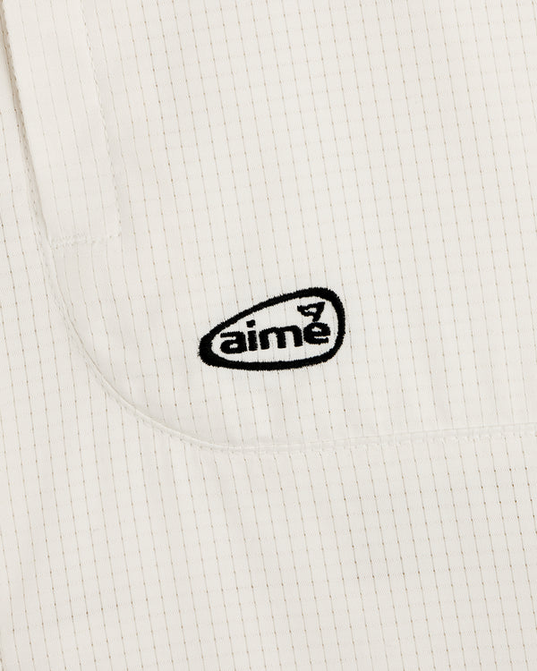Close-up of the ALD Golf Lightweight Tips Windbreaker: white fabric with thin vertical stripes and black aimé logo embroidery.