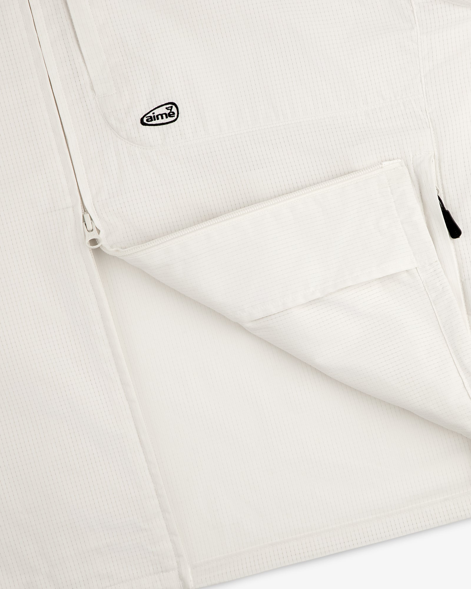 Close-up of the ALD Golf Lightweight Tips Windbreaker, featuring a white textured jacket with zip pocket and Aimé logo patch.