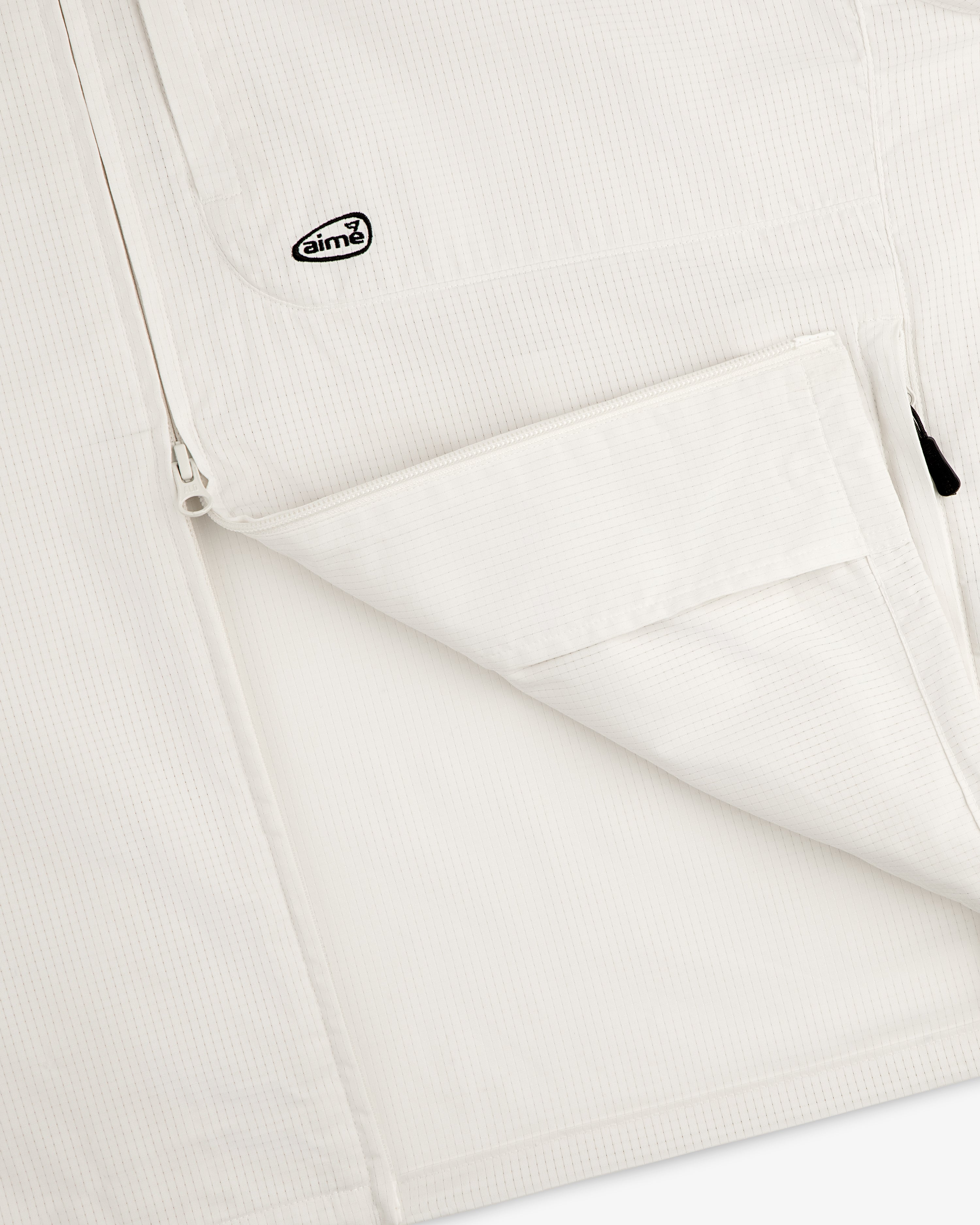 Close-up of the ALD Golf Lightweight Tips Windbreaker, featuring a white textured jacket with zip pocket and Aimé logo patch.