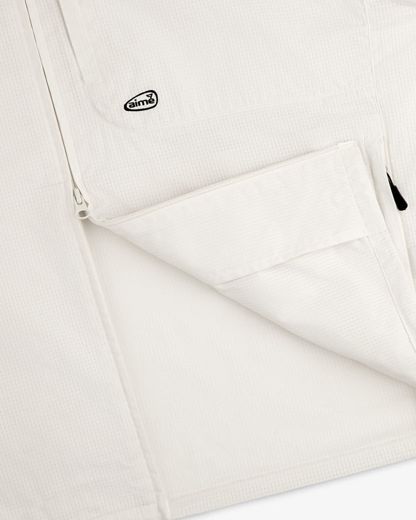 Close-up of the ALD Golf Lightweight Tips Windbreaker, featuring a white textured jacket with zip pocket and Aimé logo patch.