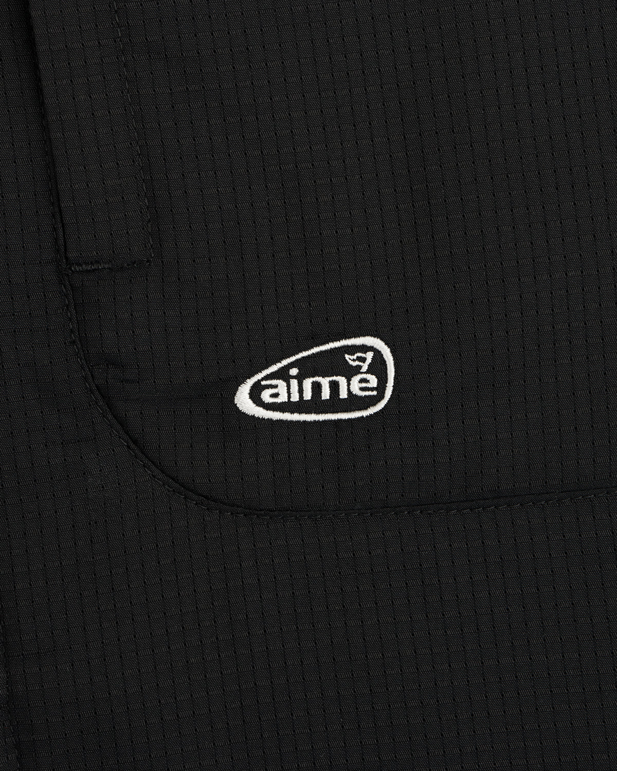 Close-up of the ALD Golf Lightweight Tips Windbreaker in black with a white aime logo embroidered on the pocket.