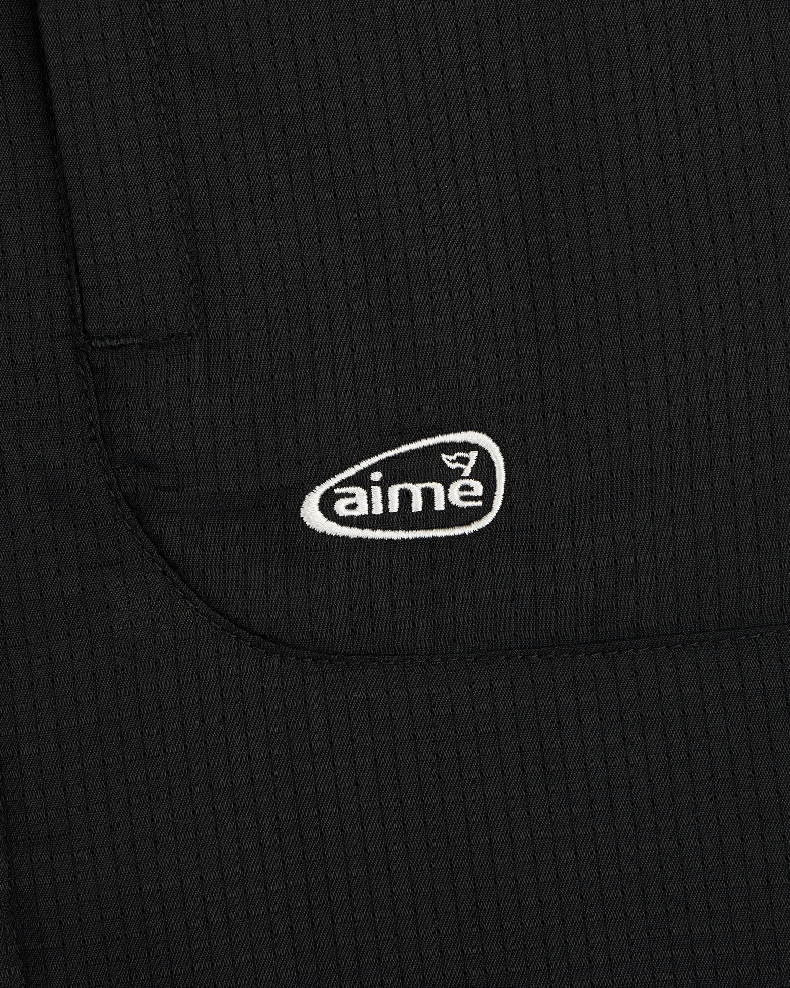 Close-up of the ALD Golf Lightweight Tips Windbreaker in black with a white aime logo embroidered on the pocket.
