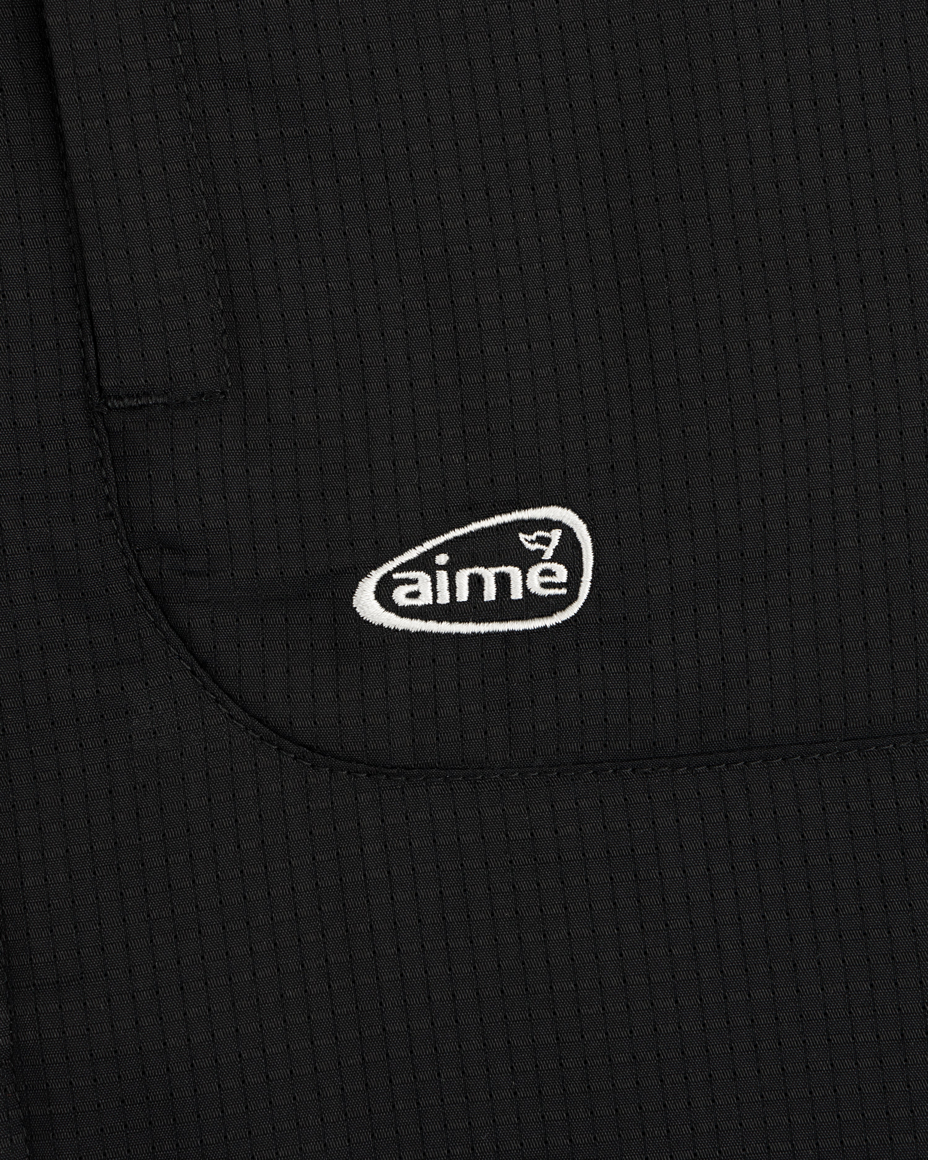 Close-up of the ALD Golf Lightweight Tips Windbreaker in black with a white aime logo embroidered on the pocket.