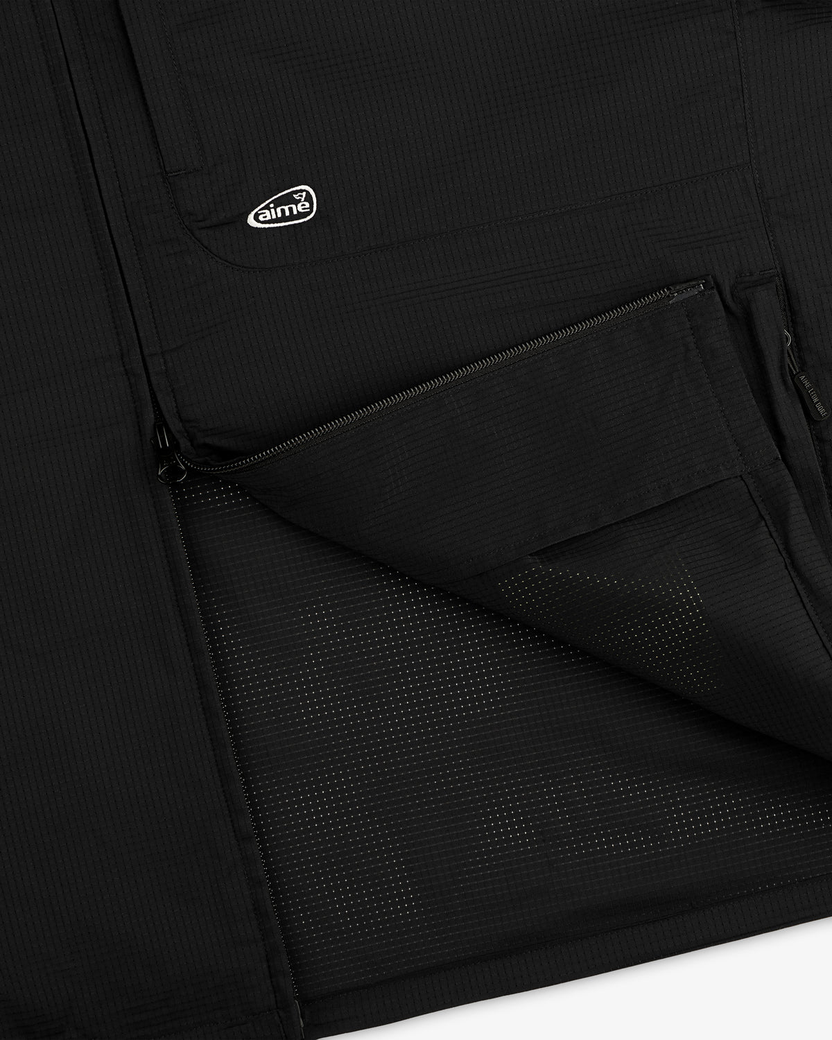 Close-up of ALD Golf Lightweight Tips Windbreaker in black with open zip pocket, mesh lining, and small aimé logo patch.
