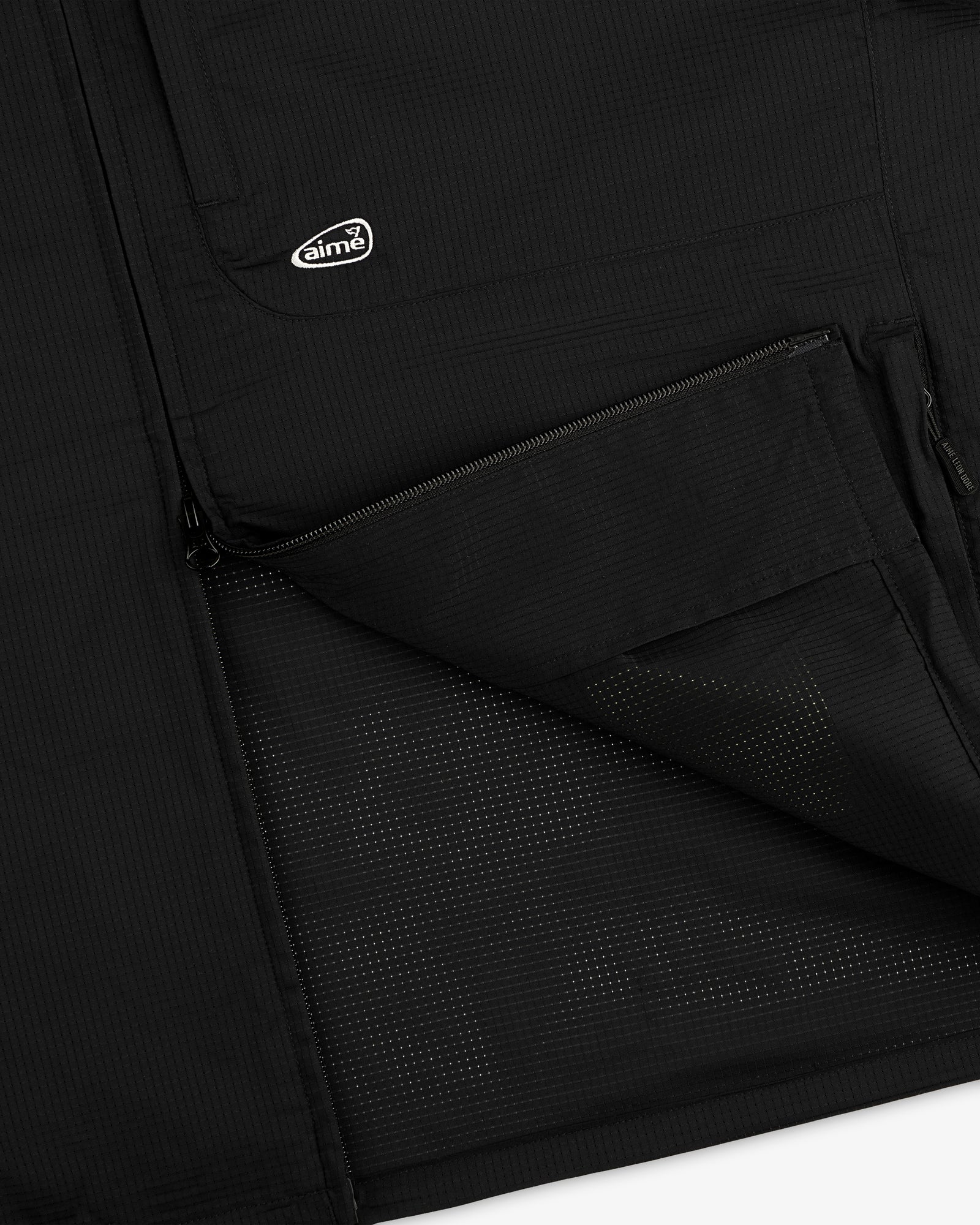 Close-up of ALD Golf Lightweight Tips Windbreaker in black with open zip pocket, mesh lining, and small aimé logo patch.
