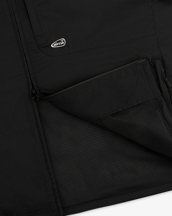Close-up of ALD Golf Lightweight Tips Windbreaker in black with open zip pocket, mesh lining, and small aimé logo patch.