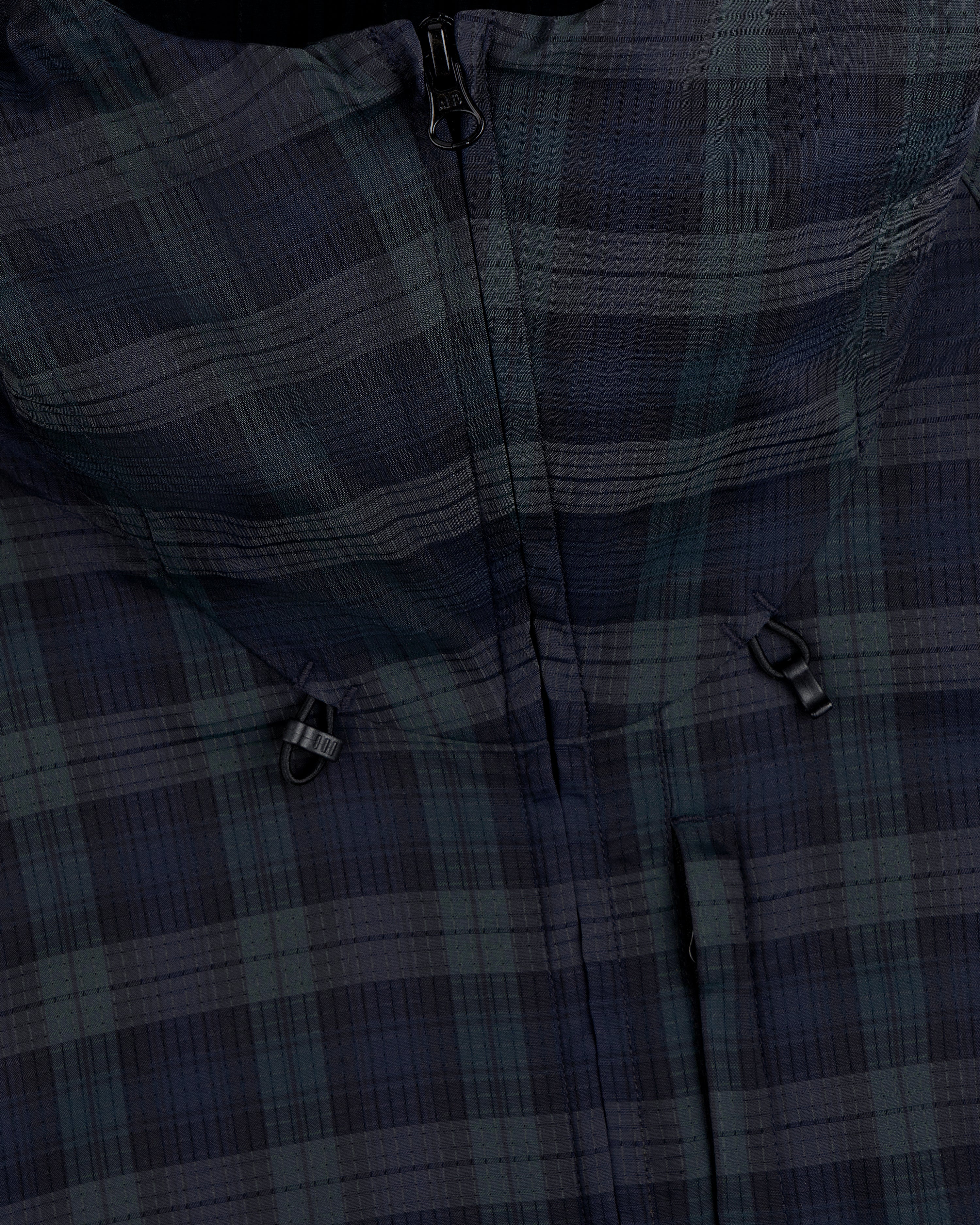 Close-up of the ALD Golf Lightweight Tips Windbreaker, featuring a plaid pattern, zipper, and two small black loops.