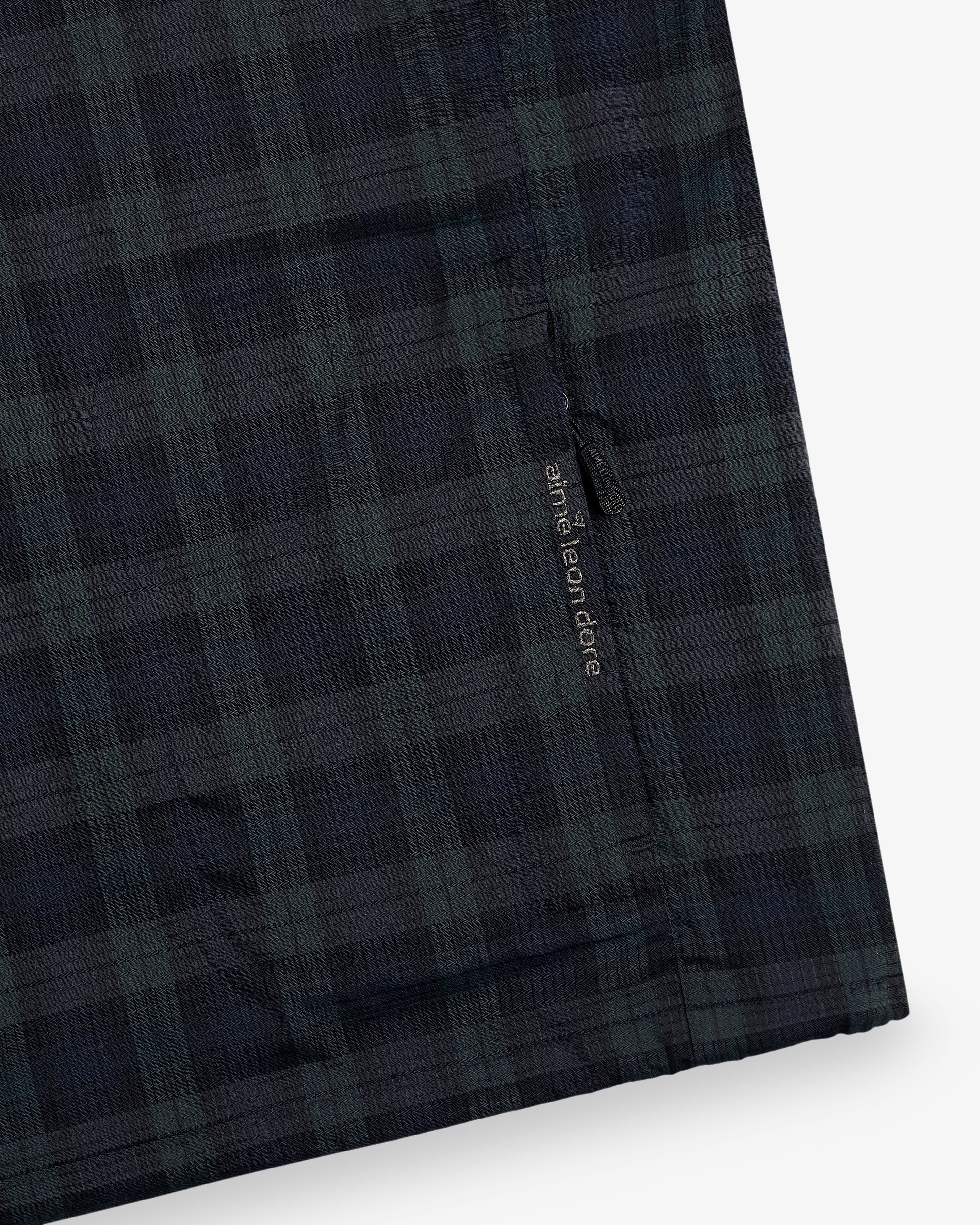Close-up of the ALD Golf Lightweight Tips Windbreaker in dark blue and green plaid with a small black "and wander" tag.