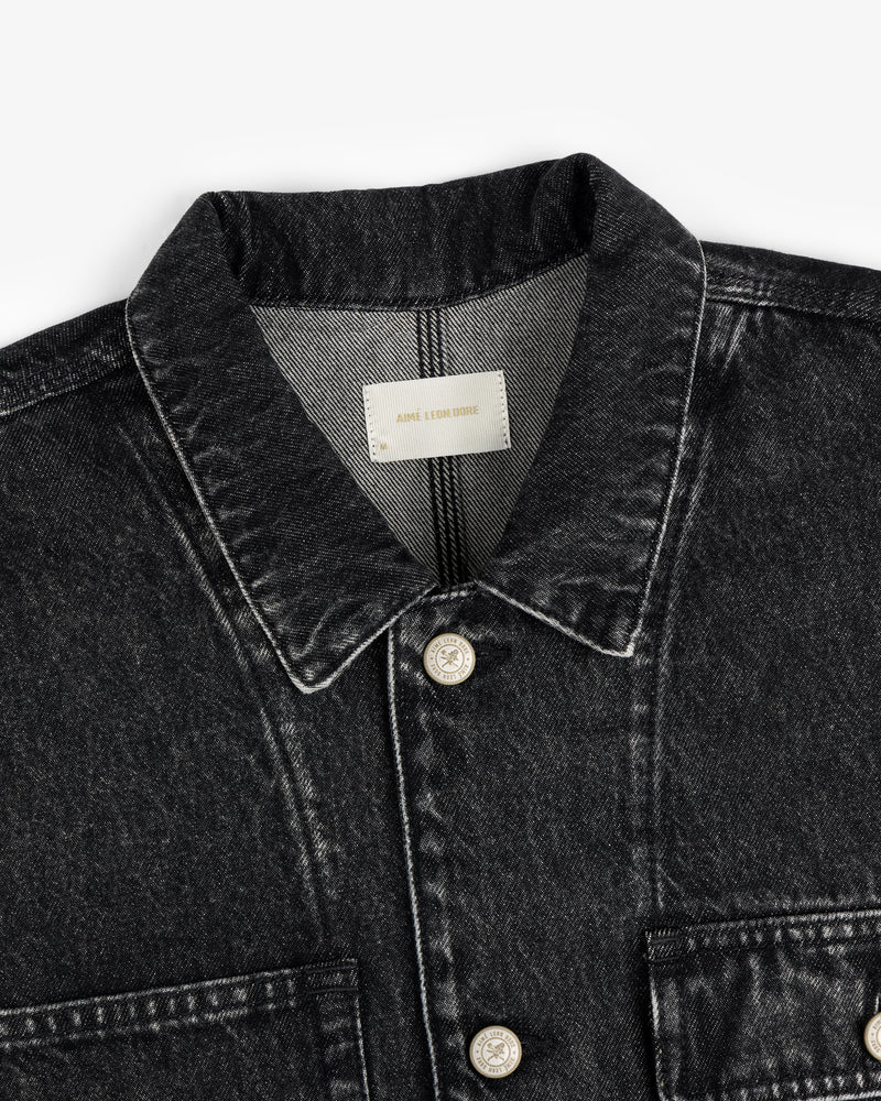 Close-up of a black Denim Trucker Jacket with a collar, silver buttons, and a visible beige label inside the neckline.