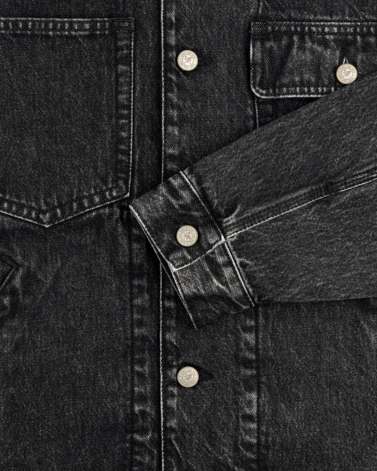 Close-up of Denim Trucker Jacket in black with silver buttons, chest pockets, and visible stitching.