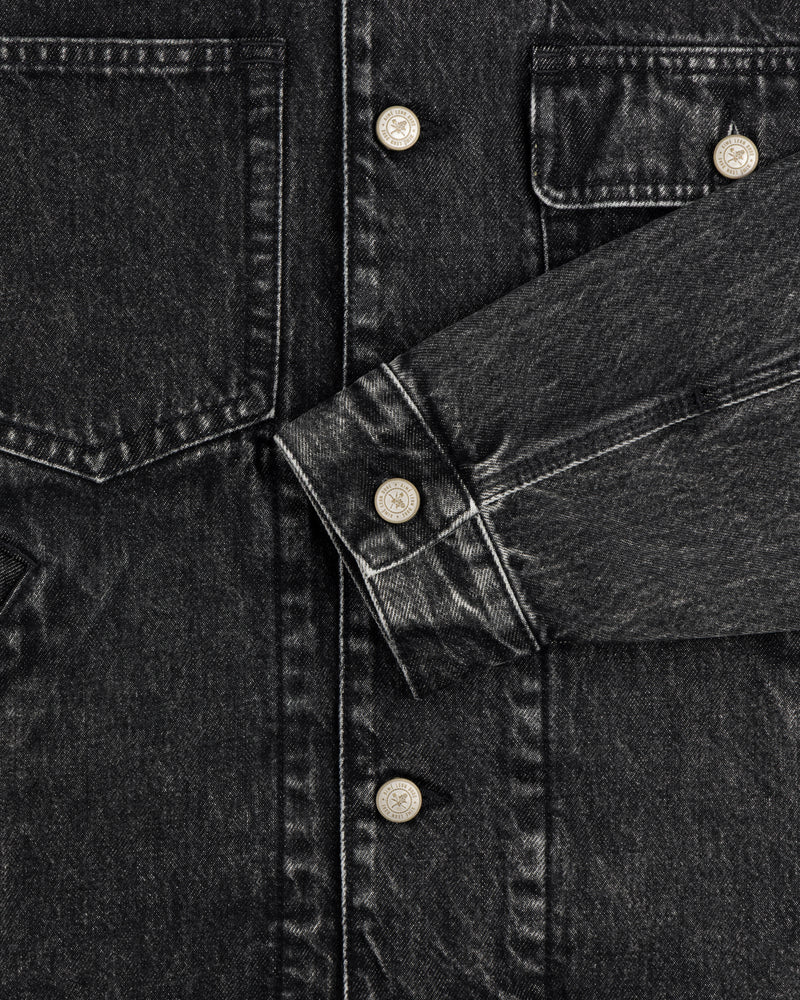 Close-up of Denim Trucker Jacket in black with silver buttons, chest pockets, and visible stitching.