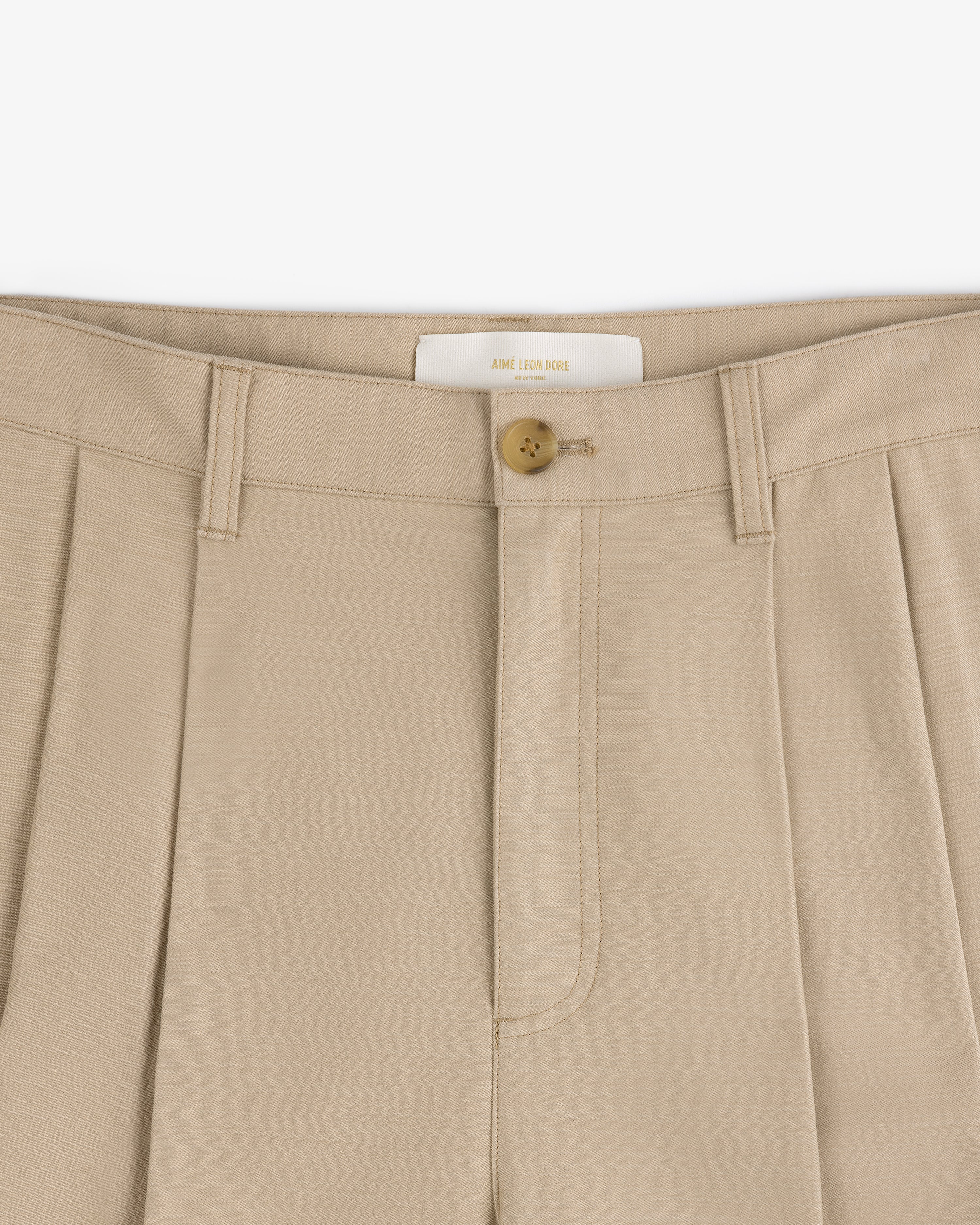 Close-up of Double Pleated Pant in beige featuring a button closure and detailed waistband.