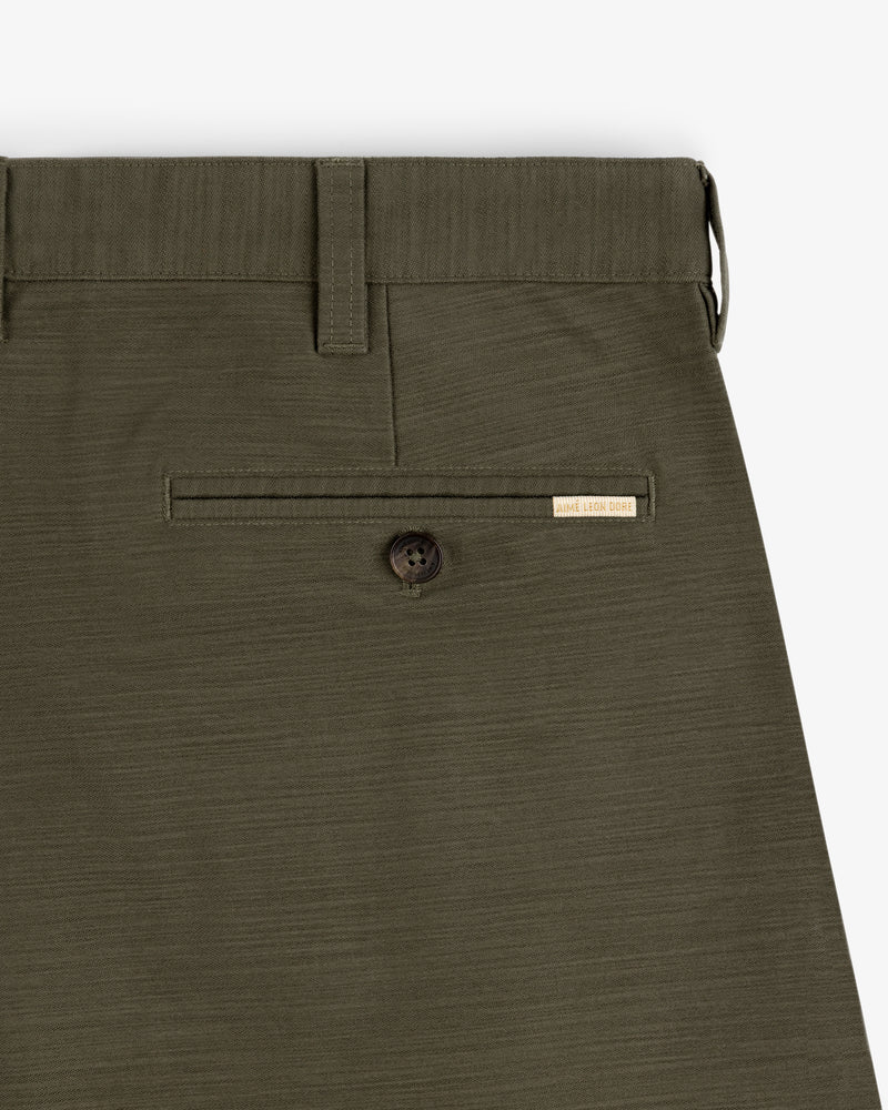 Close-up of Double Pleated Pant in olive green with a back buttoned pocket and small beige label above the pocket.