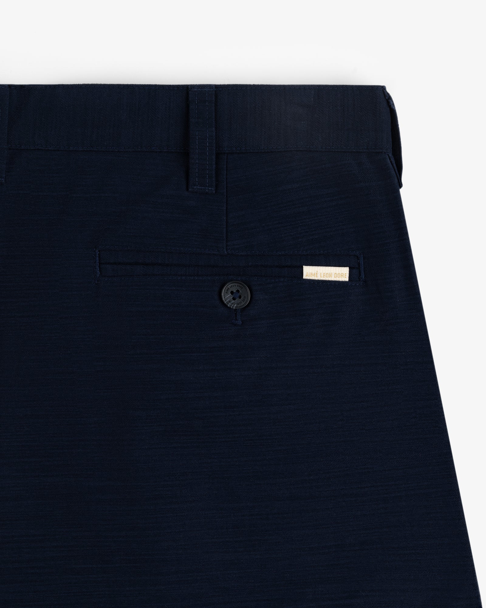 Close-up of Double Pleated Pant's navy blue pocket with a button and a small beige label above it.