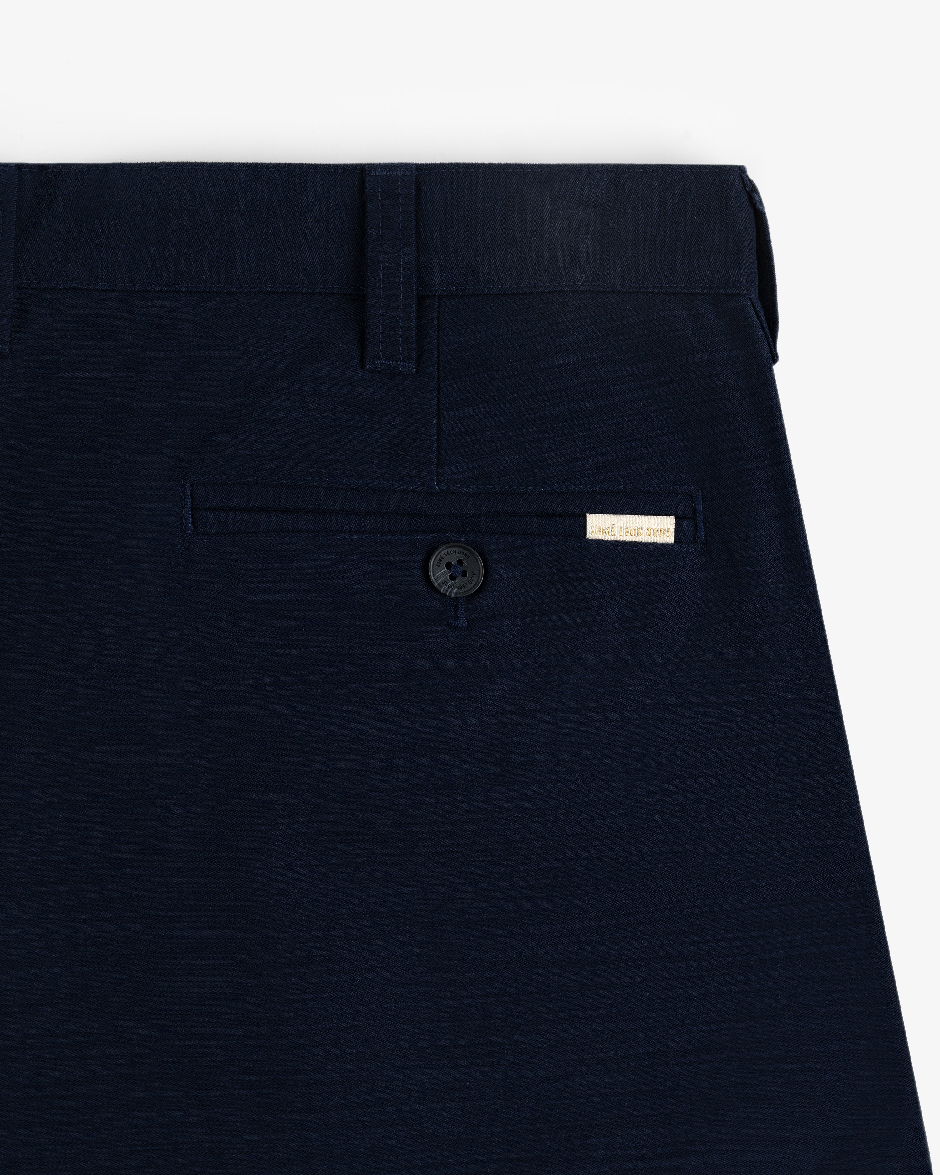 Close-up of Double Pleated Pant's navy blue pocket with a button and a small beige label above it.