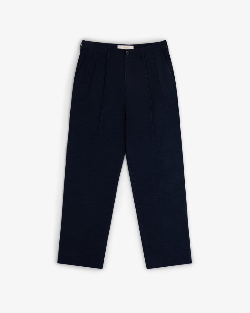 Double Pleated Pant in navy blue with button and zip closure, shown laid flat on a white background.