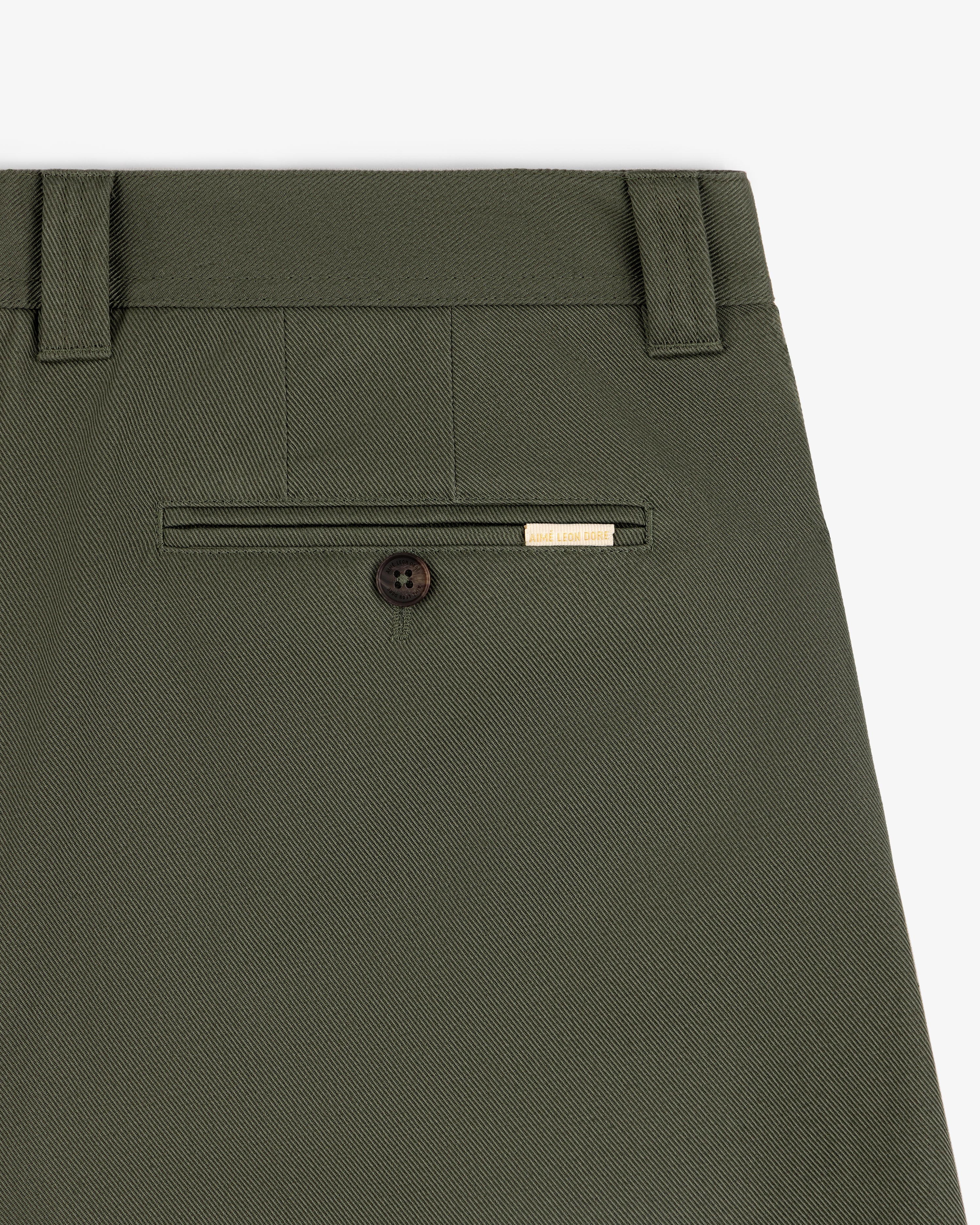 Close-up of Officer Pant in olive green, featuring a back pocket with button and a small gold label above it.