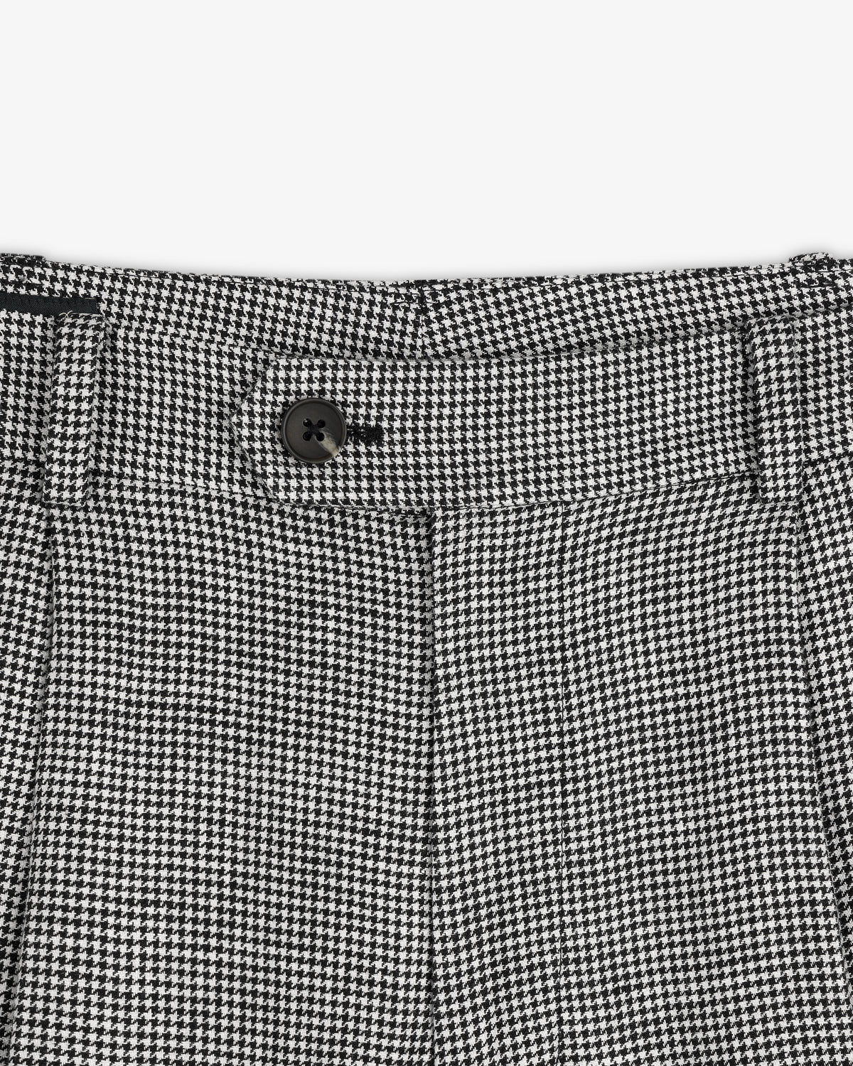 Close-up of the Houndstooth Pleated Trouser's black and white houndstooth waistband with a black button.