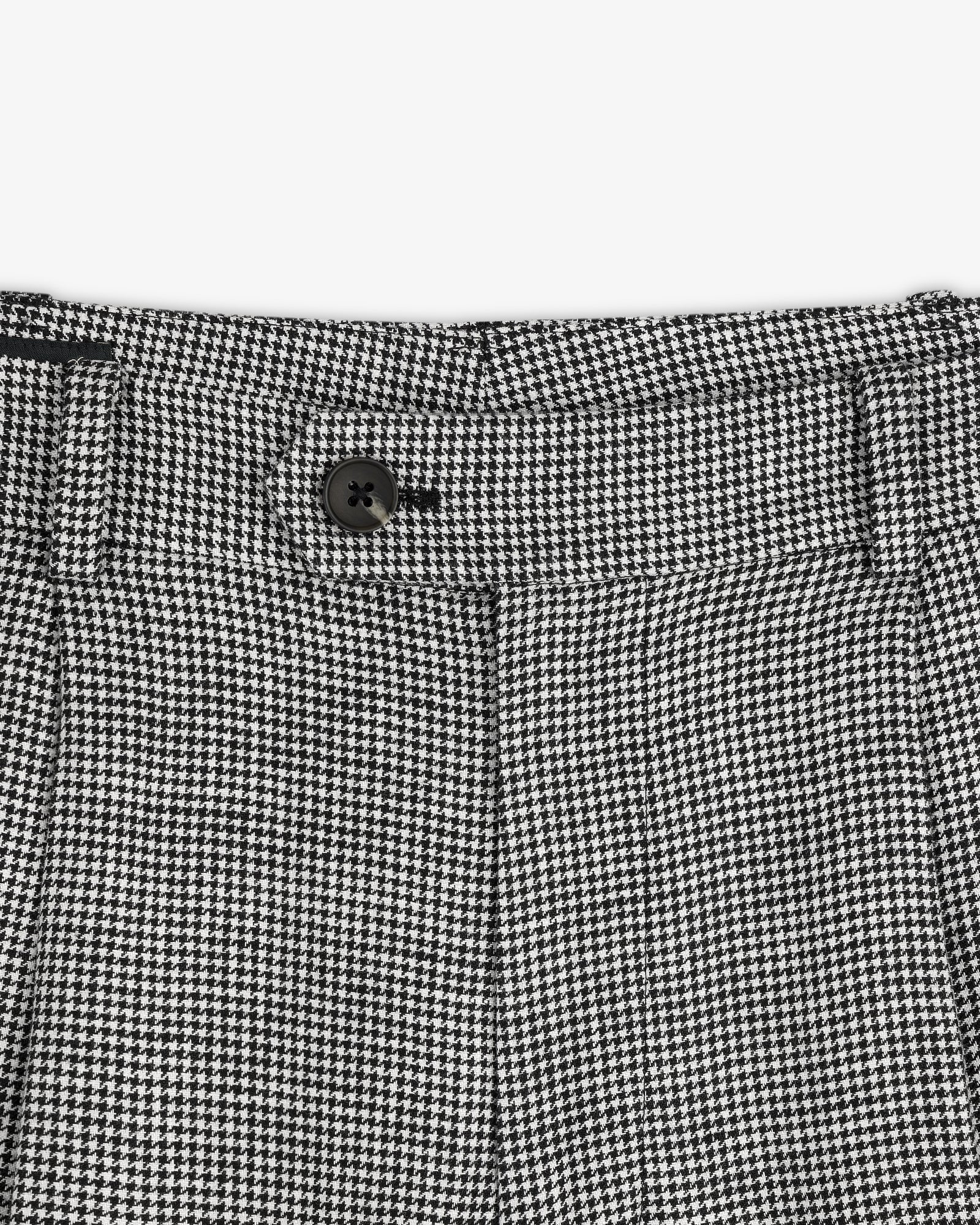 Close-up of the Houndstooth Pleated Trouser's black and white houndstooth waistband with a black button.