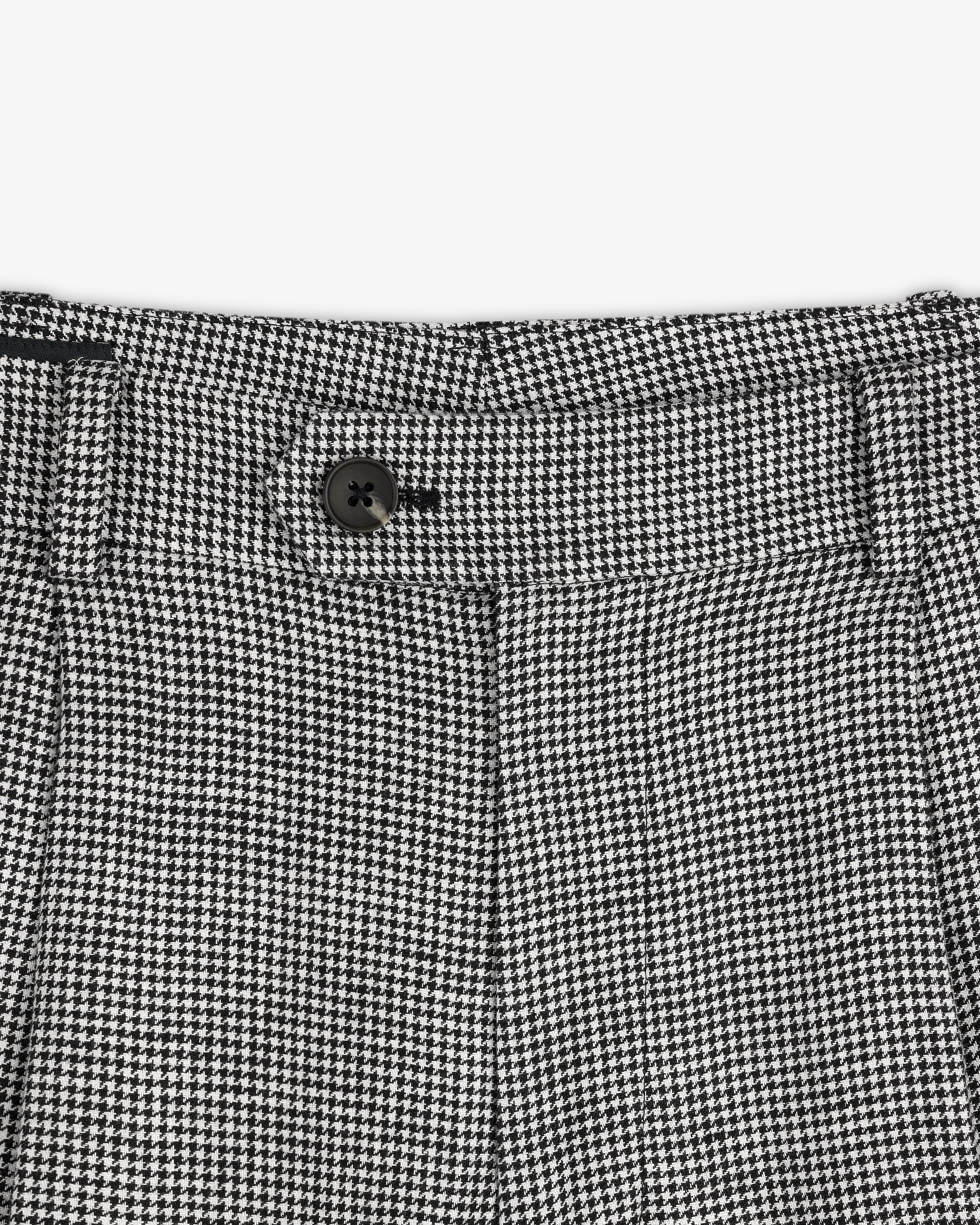 Close-up of the Houndstooth Pleated Trouser's black and white houndstooth waistband with a black button.