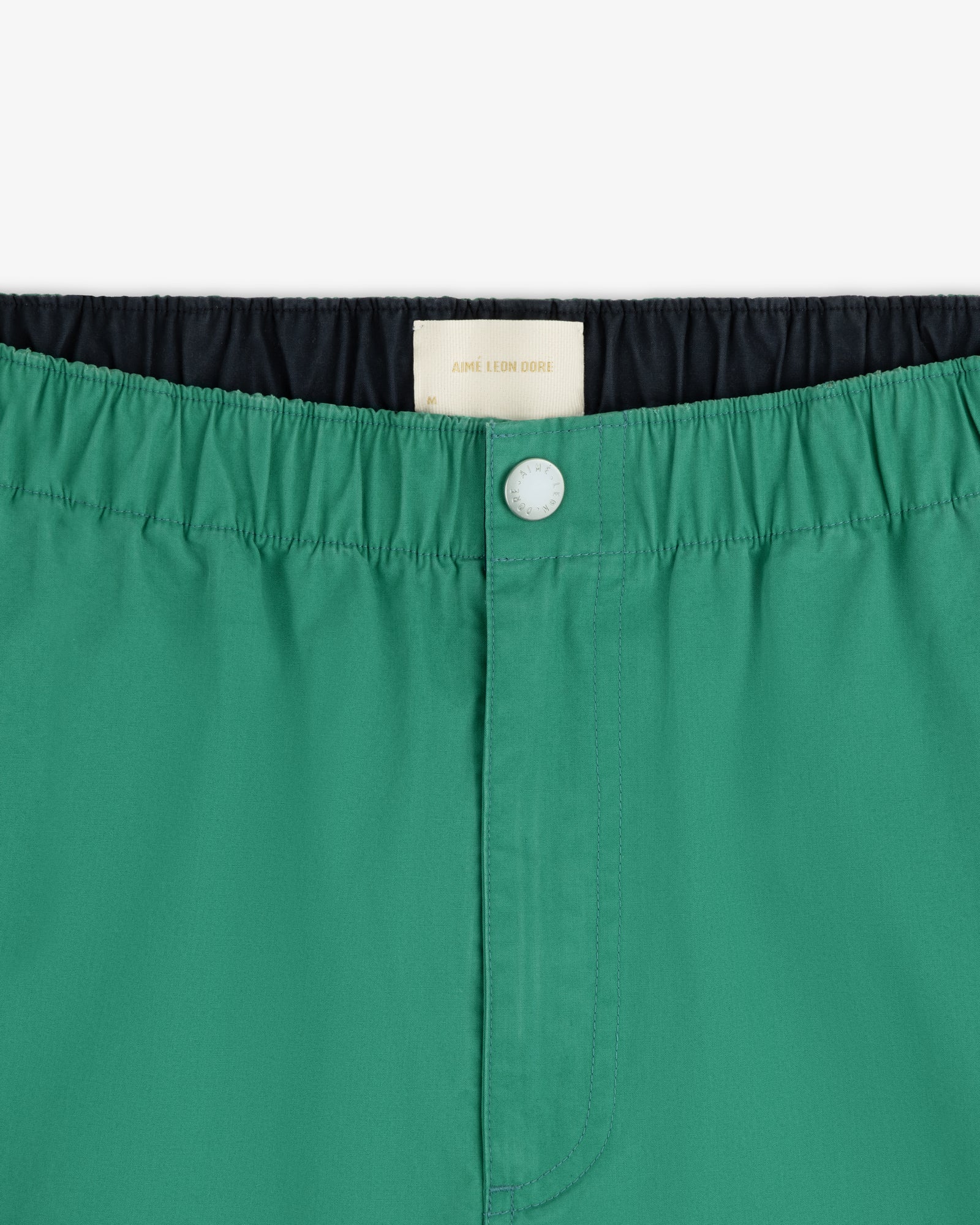 Close-up of Washed Cotton Windbreaker Pant in green with elastic waistband, white button, and inner label visible.