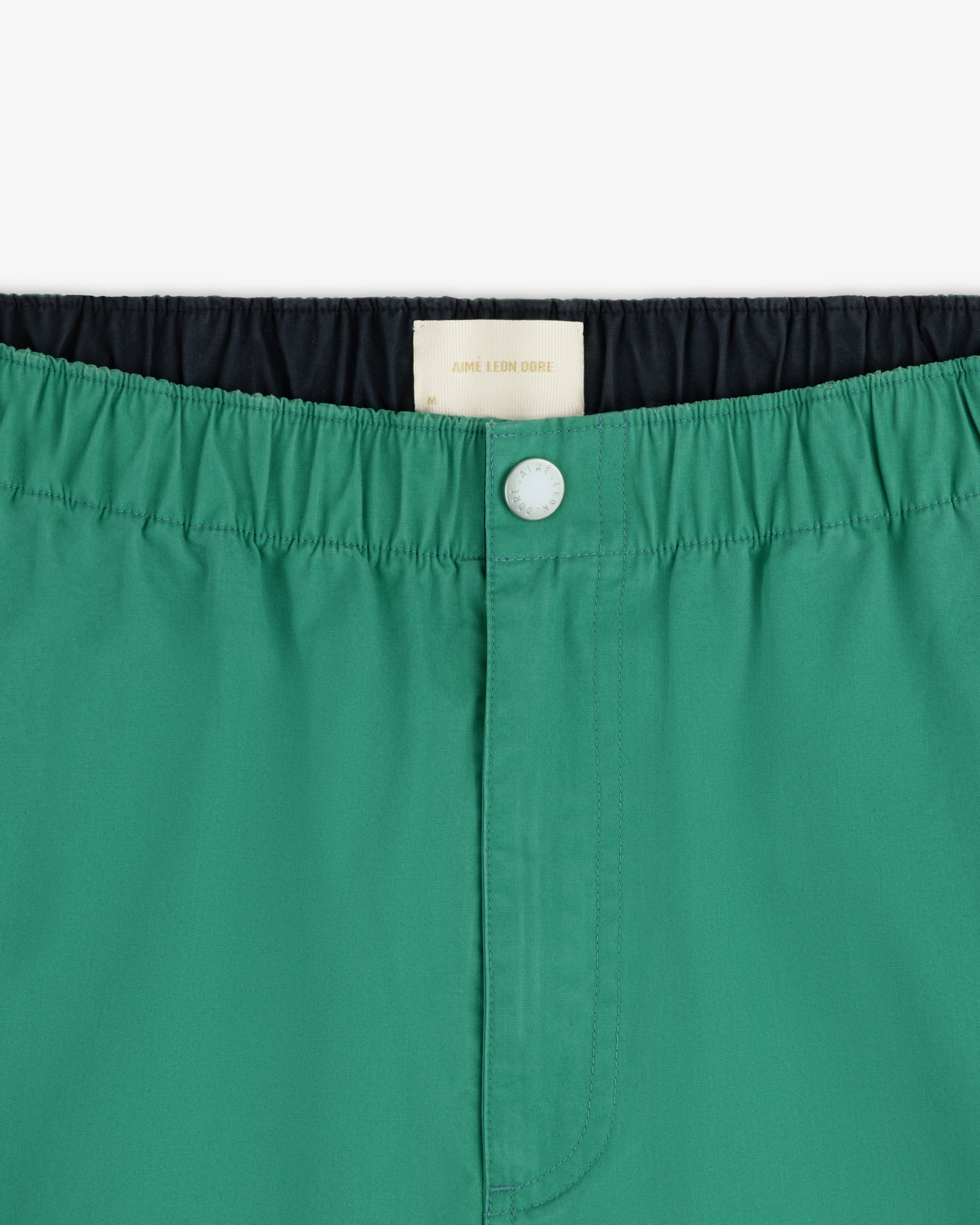Close-up of Washed Cotton Windbreaker Pant in green with elastic waistband, white button, and inner label visible.