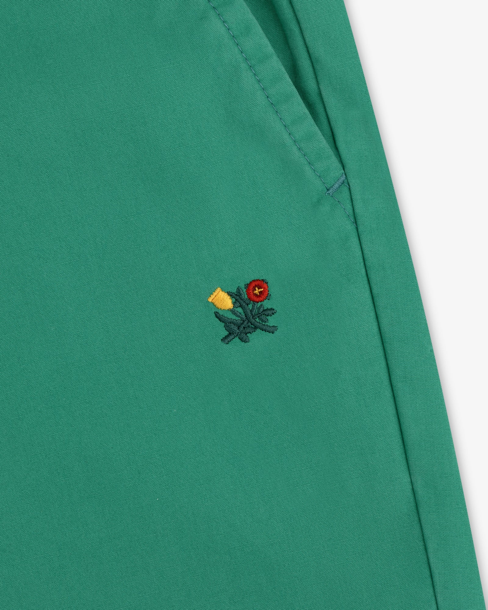Washed Cotton Windbreaker Pant in green with visible stitching and a small embroidered floral detail near the seam.