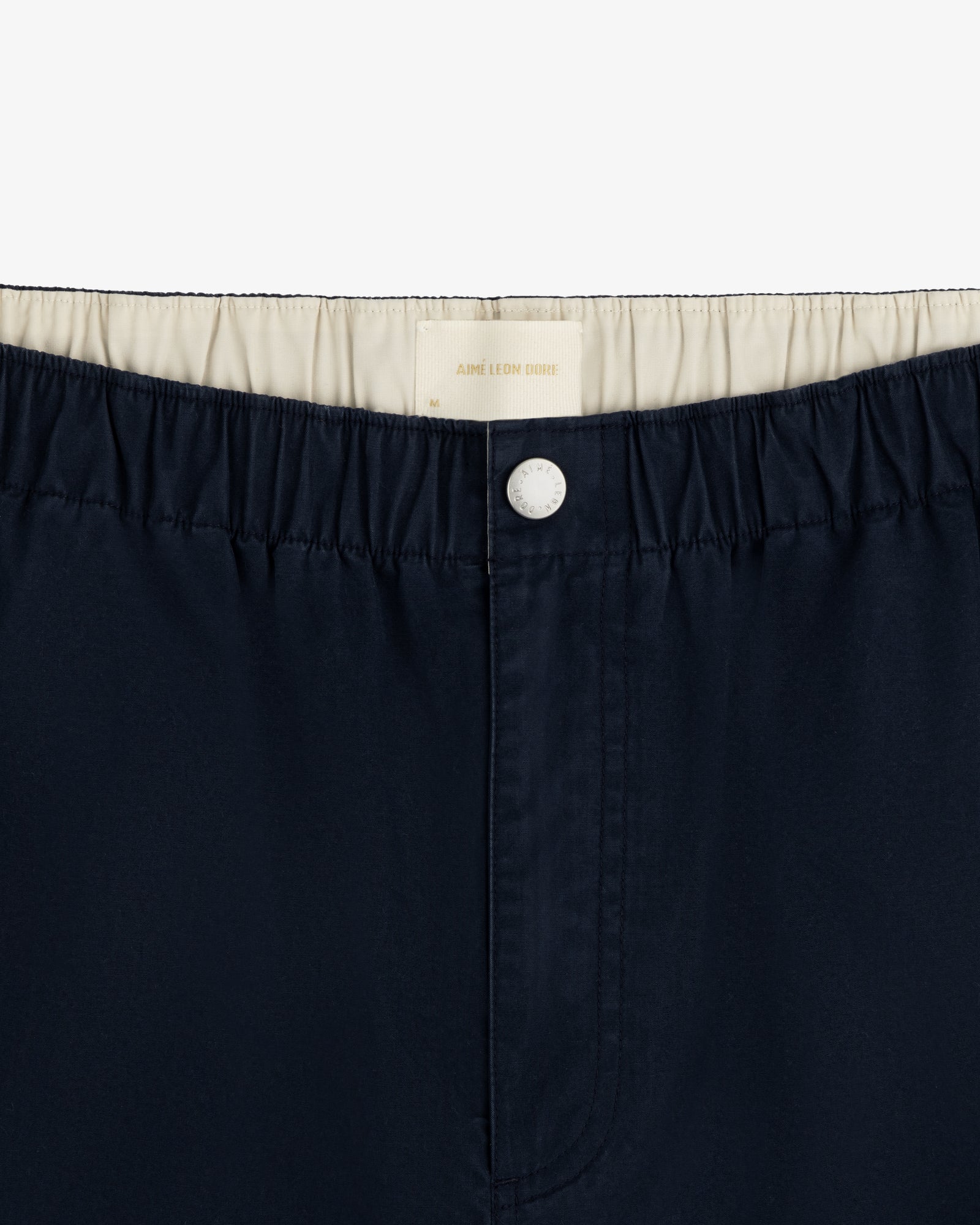 Close-up of Washed Cotton Windbreaker Pant in navy blue with elastic waistband, white lining, and top white button.