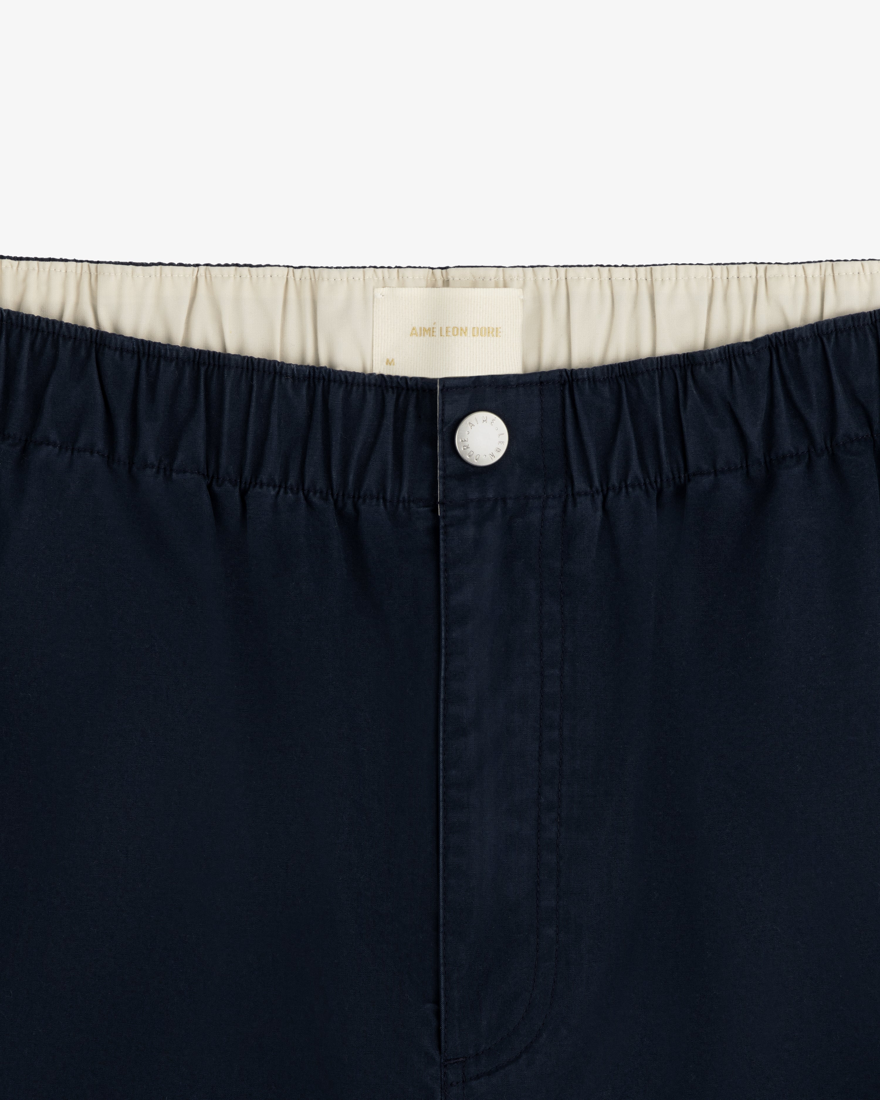 Close-up of Washed Cotton Windbreaker Pant in navy blue with elastic waistband, white lining, and top white button.