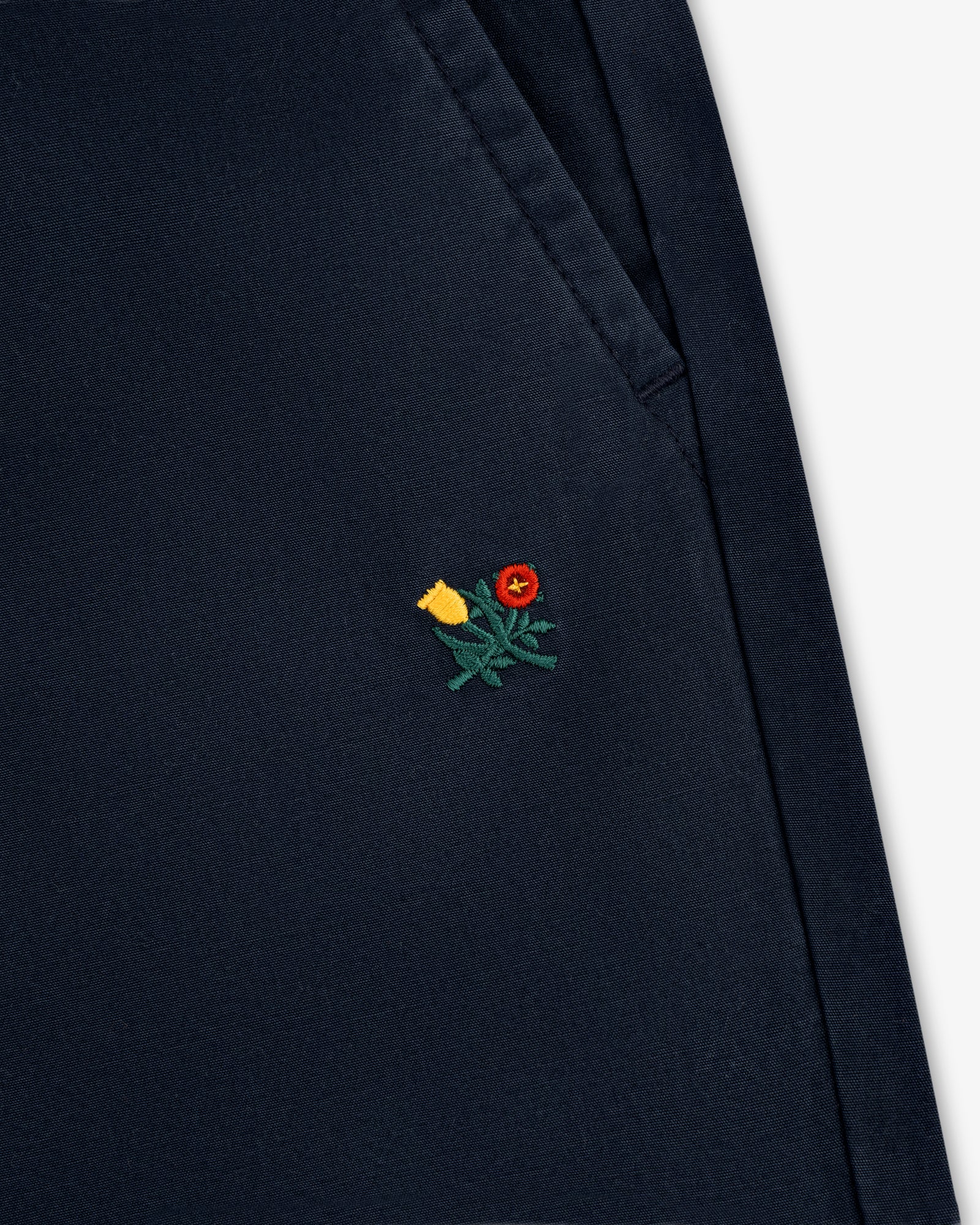 Close-up of Washed Cotton Windbreaker Pant in navy with a small yellow and red flower embroidered near the pocket seam.