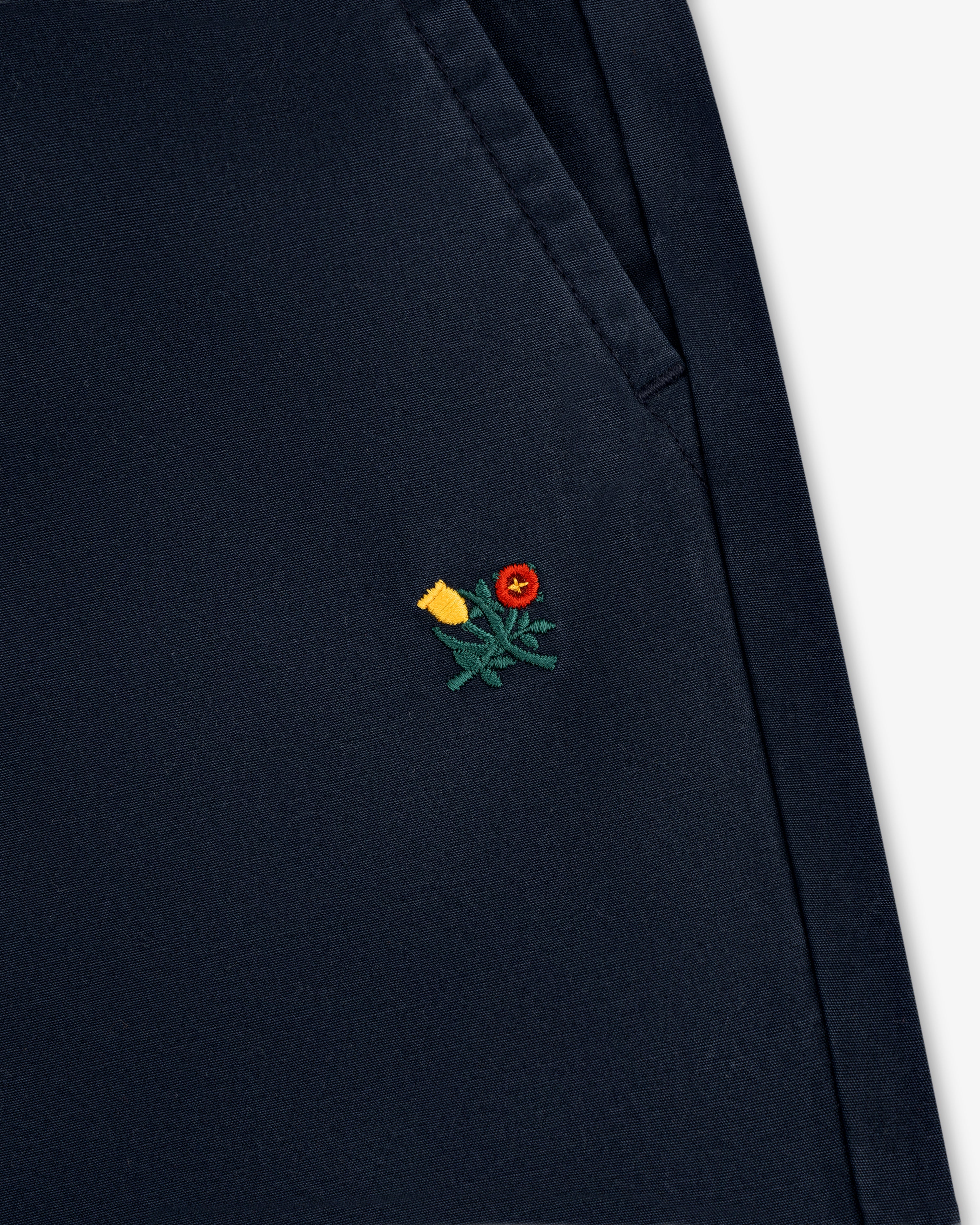 Close-up of Washed Cotton Windbreaker Pant in navy with a small yellow and red flower embroidered near the pocket seam.