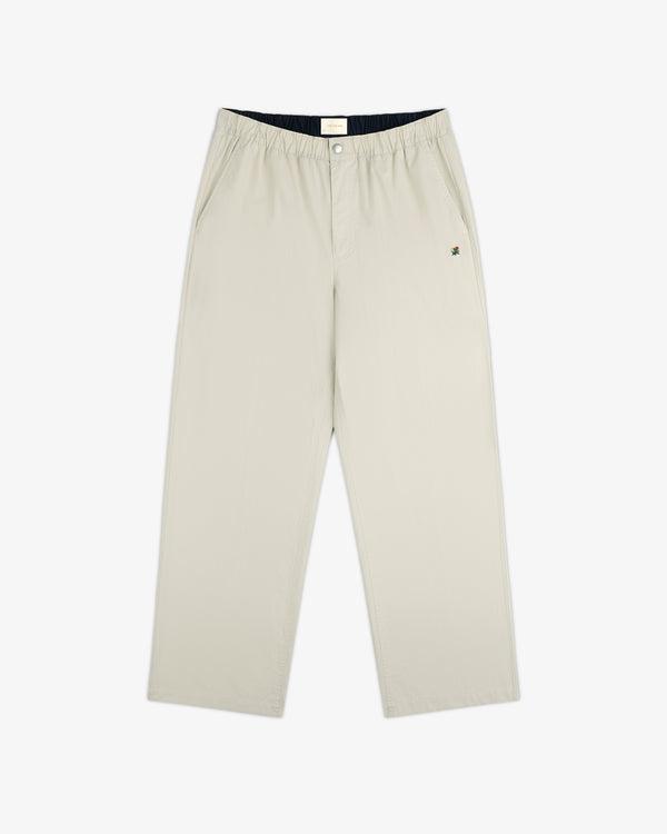 The Washed Cotton Windbreaker Pant features a beige, wide-leg design with an elastic waistband and side pockets.