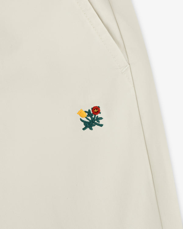 Close-up of Washed Cotton Windbreaker Pant fabric with a small red embroidered flower and green leaves near a seam.