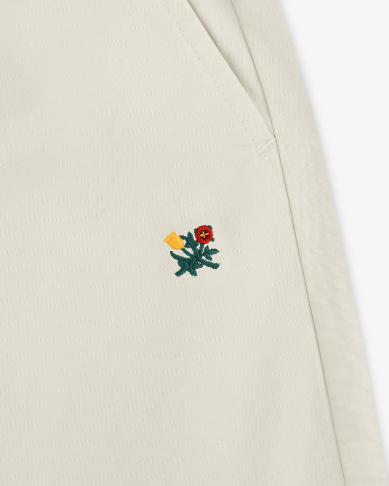 Close-up of Washed Cotton Windbreaker Pant fabric with a small red embroidered flower and green leaves near a seam.