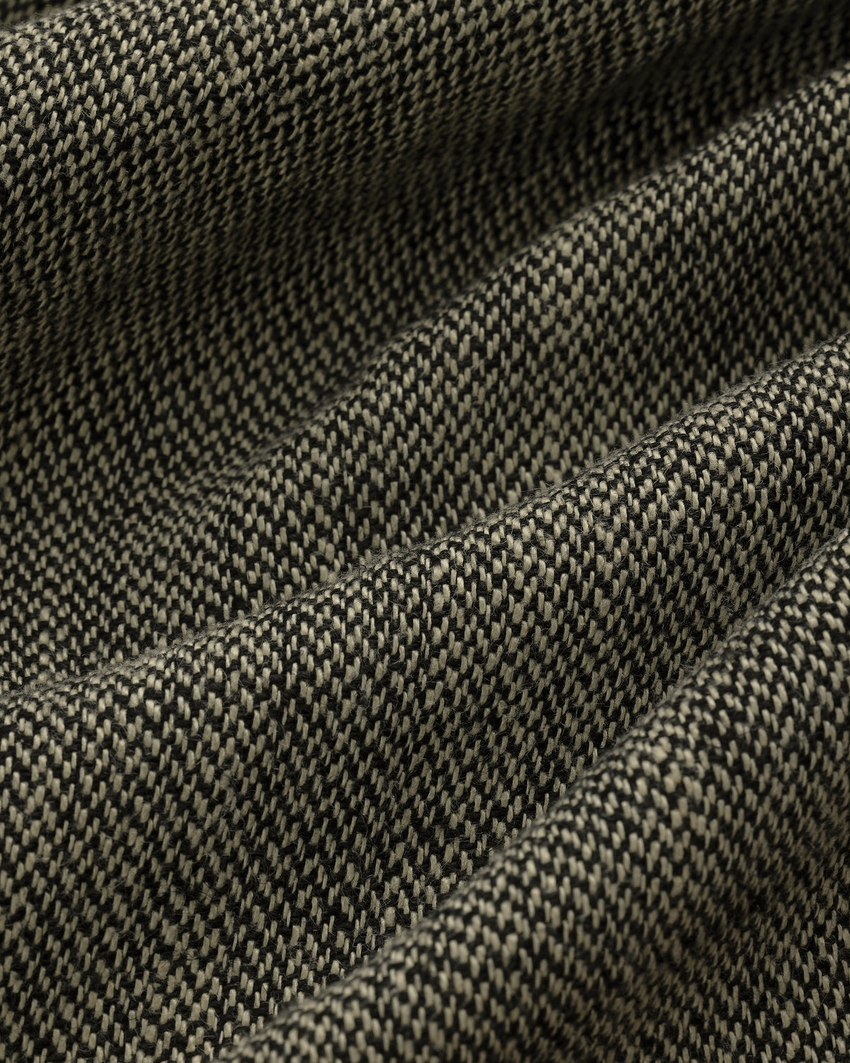 Close-up of textured black and beige Yarn Dyed Linen Suit Trouser fabric, showing folds and a subtle pattern.