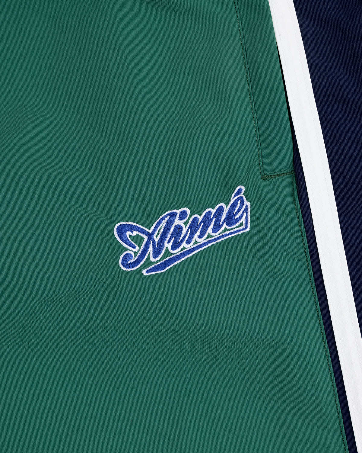 Green Colorblock Track Pant featuring Aimé embroidered in blue and white script beside white and navy stripes.