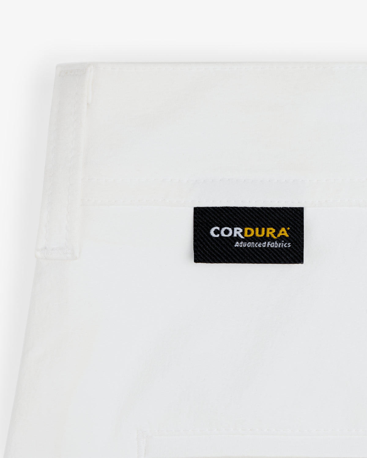 Close-up of ALD Golf Cordura Double Pleated Pant featuring a black CORDURA Advanced Fabrics label on white fabric.