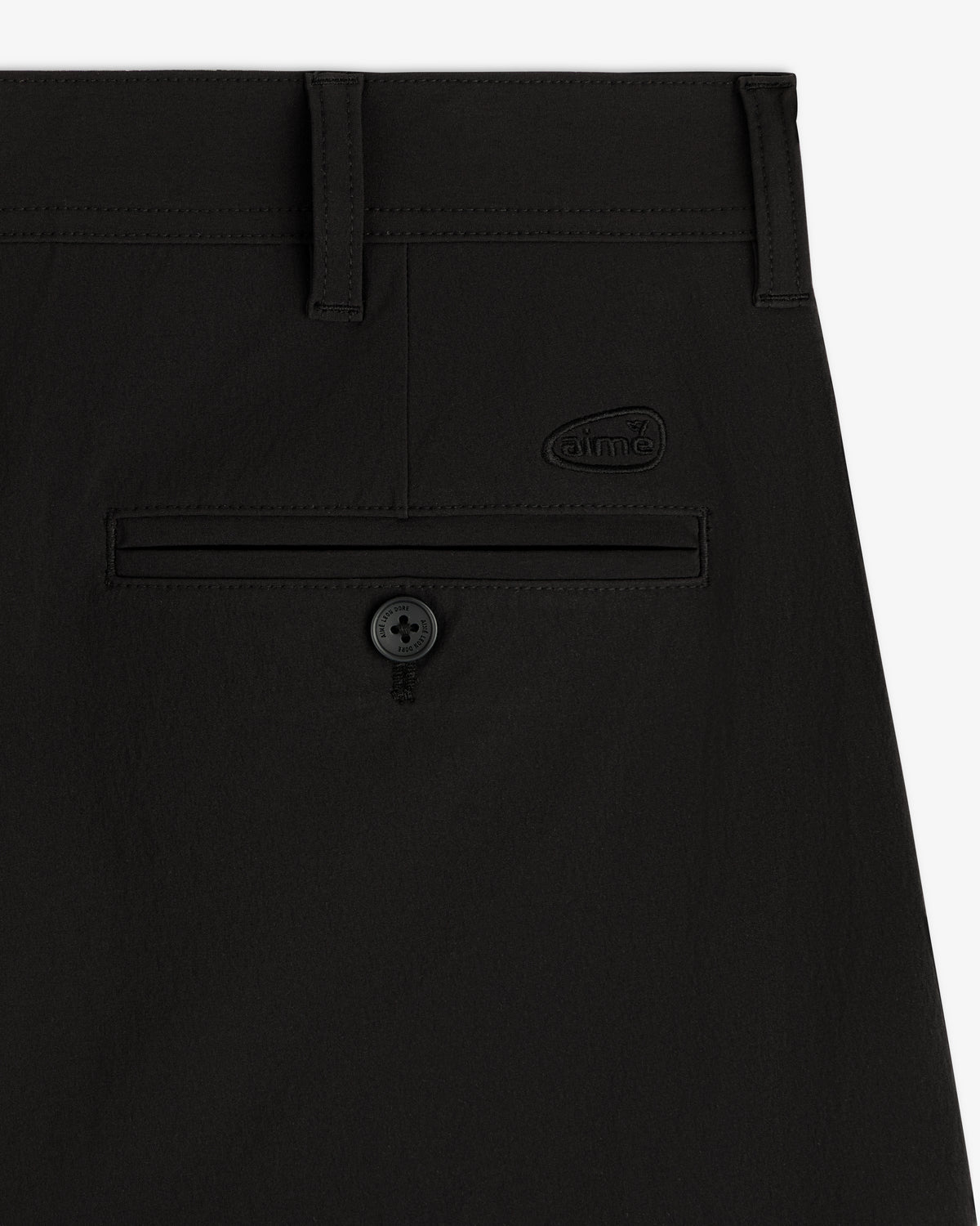 Close-up of ALD Golf Cordura Double Pleated Pant in black with a back pocket, button, and small dime logo above.